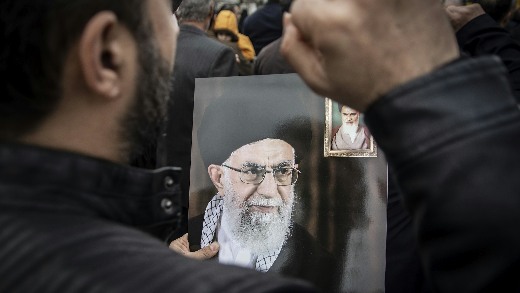 RASHT, GILAN, IRAN - 2020/01/03: A man protesting the killing of General Qasem Soleimani while carrying a poster of Iran's leader, Ali Khamenei. After the killing of General Qasem Soleimani, commander of Quds Force by the US Army in Iraq, people throughout Iran and the city of Rasht mourned him on the streets. (Photo by Babak Jeddi/SOPA Images/LightRocket via Getty Images)