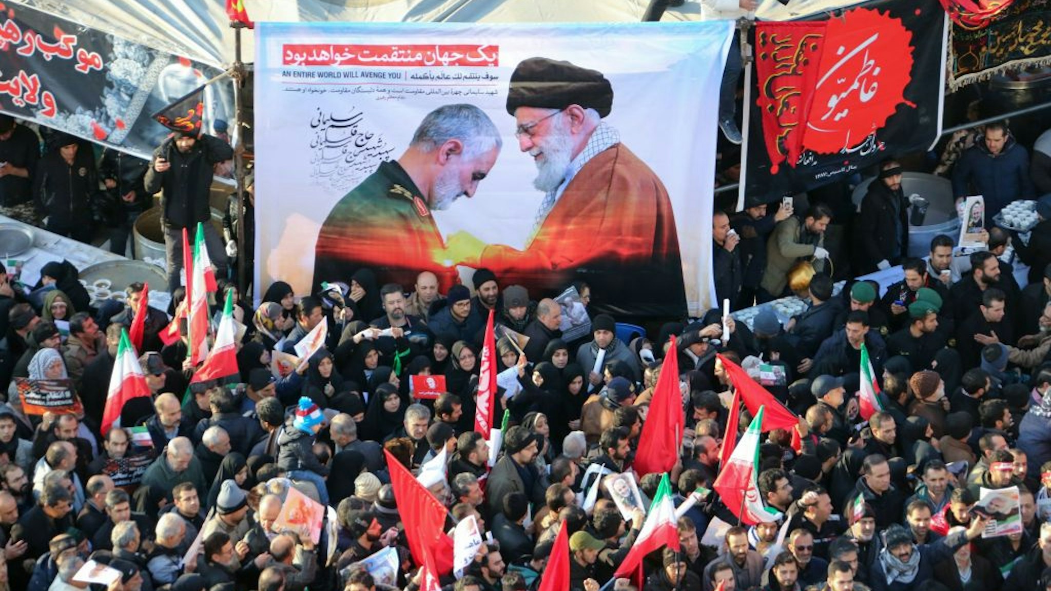 Iranian mourners carry a picture of Iran's Supreme Leader Ayatollah Ali Khamenei (R) granting the Order of Zolfaghar, the highest military honour of Iran, to General Qasem Soleimani, during the latter's funeral procession in the capital Tehran on January 6, 2020. - Downtown Tehran was brought to a standstill as mourners flooded the Iranian capital to pay an emotional homage to Soleimani, the "heroic" general who spearheaded Iran's Middle East operations as commander of the Revolutionary Guards' Quds Force and was killed in a US drone strike on January 3 near Baghdad airport along with Iraqi paramilitary chief Abu Mahdi al-Muhandis and others.