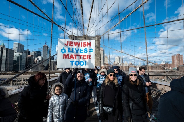 MANHATTAN, NY - JANUARY 05: A young marcher walking across the Brooklyn Bridge carrying a handmade sign that says "Jewish Lives Matter Too" with a Jewish star with the Brooklyn Bridge Arch and the Freedom Tower behind them. This was part of the effort to support the No Hate No Fear Jewish Solidarity March which started in Foley Square in the Manhattan borough of New York and walked across the Brooklyn Bridge to raise awareness of no tolerance for violence against Jewish people. The March was held on January 01, 2020, USA.