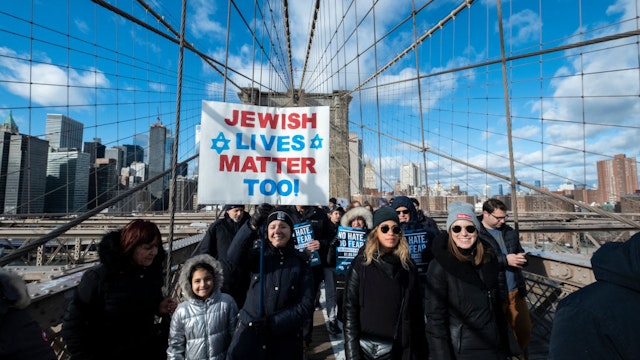 MANHATTAN, NY - JANUARY 05: A young marcher walking across the Brooklyn Bridge carrying a handmade sign that says "Jewish Lives Matter Too" with a Jewish star with the Brooklyn Bridge Arch and the Freedom Tower behind them. This was part of the effort to support the No Hate No Fear Jewish Solidarity March which started in Foley Square in the Manhattan borough of New York and walked across the Brooklyn Bridge to raise awareness of no tolerance for violence against Jewish people. The March was held on January 01, 2020, USA.