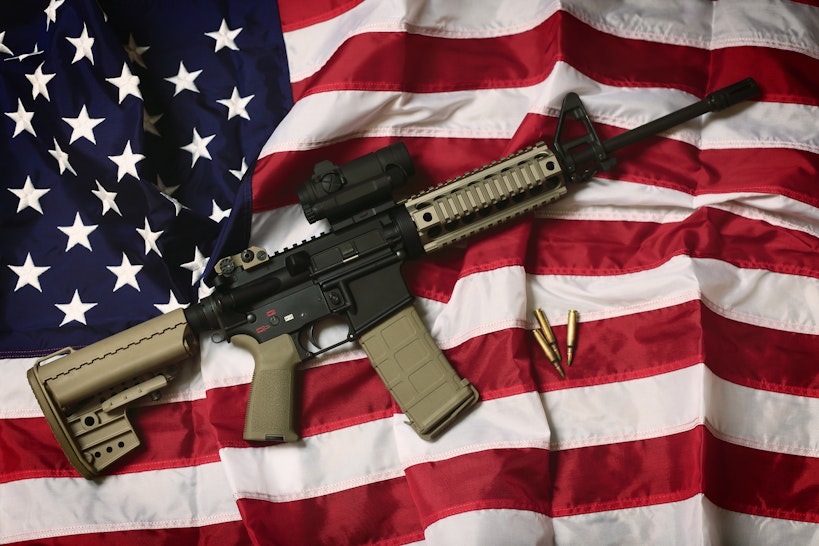 An AR-15 rifle with bullets on an American flag, a symbol of the right of patriotic Americans to bear arms, guaranteed by the Second Amendment.
