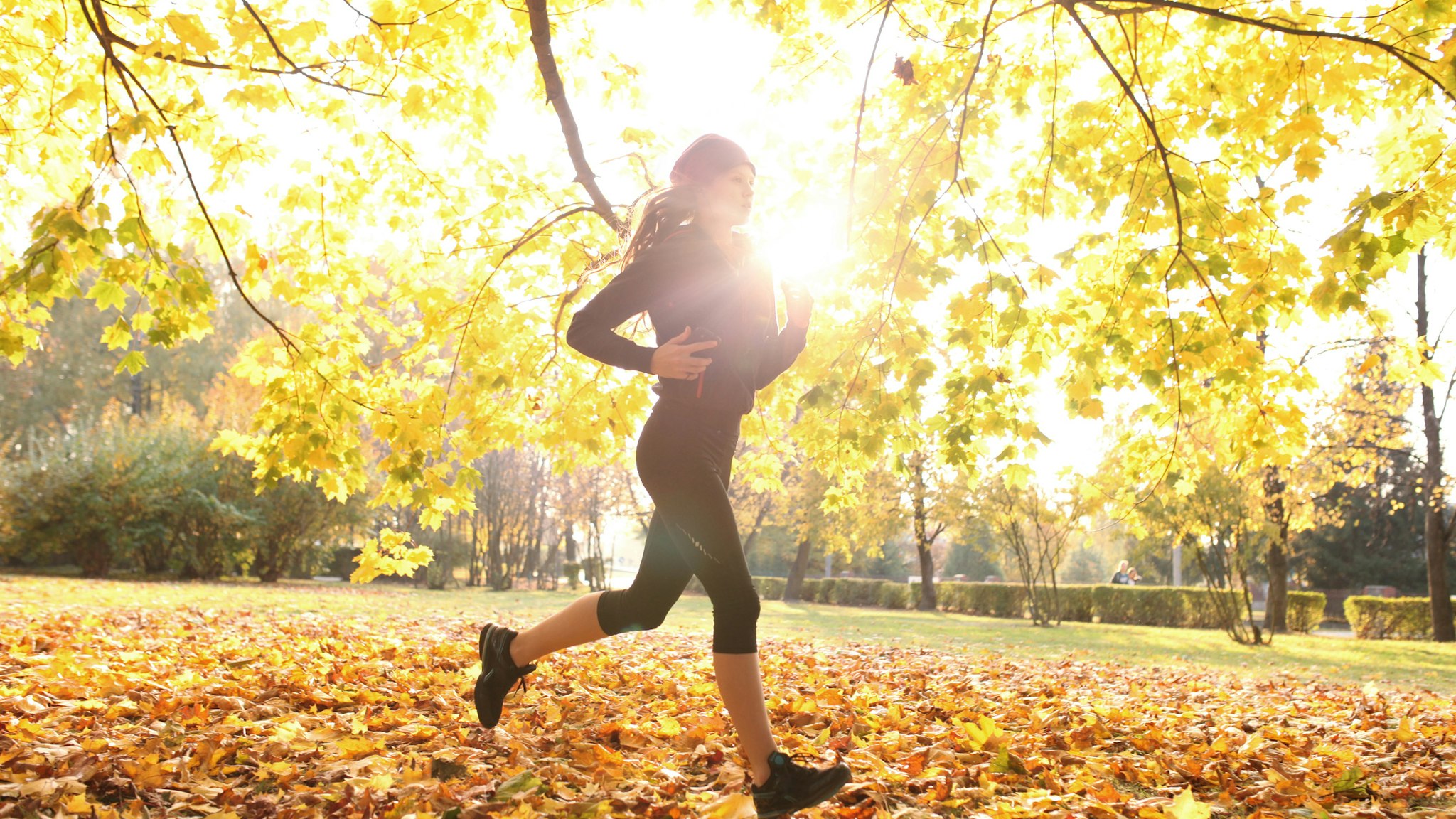 Female athlete on training run through fall leaves, city park