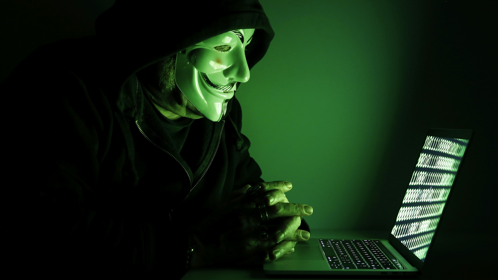 PARIS, FRANCE - DECEMBER 27: In this photo illustration, a hacker with an Anonymous mask on his face and a hood on his head uses a computer on December 27, 2019 in Paris, France. In IT security, a hacker is an IT specialist, who is looking for ways to bypass software and hardware protections. Hackers are generally intelligent programmers who seek to manipulate or modify a computer system or network.