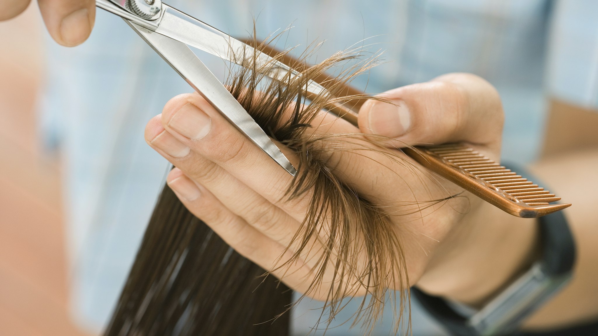 Hairdresser cutting woman's hair in salon, focus on hair, hands and scissors, close-up