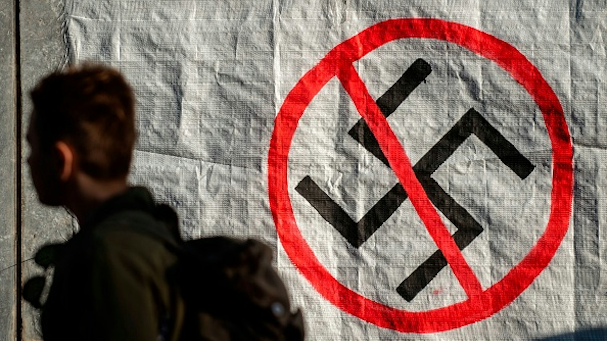 A man walks next to a logo of Nazi swastika during an anti-fascist rally outside the Court of Appeal during the testify of former MP and leader of Golden Dawn party Nikolaos Michaloliakos, on November 6, 2019, in Athens. - The 61-year-old Holocaust denier is one of nearly 70 defendants facing sentences of five to 20 years in prison. The main charge against them is participation in a criminal organisation, in addition to a host of other indictments related to murder and assault.