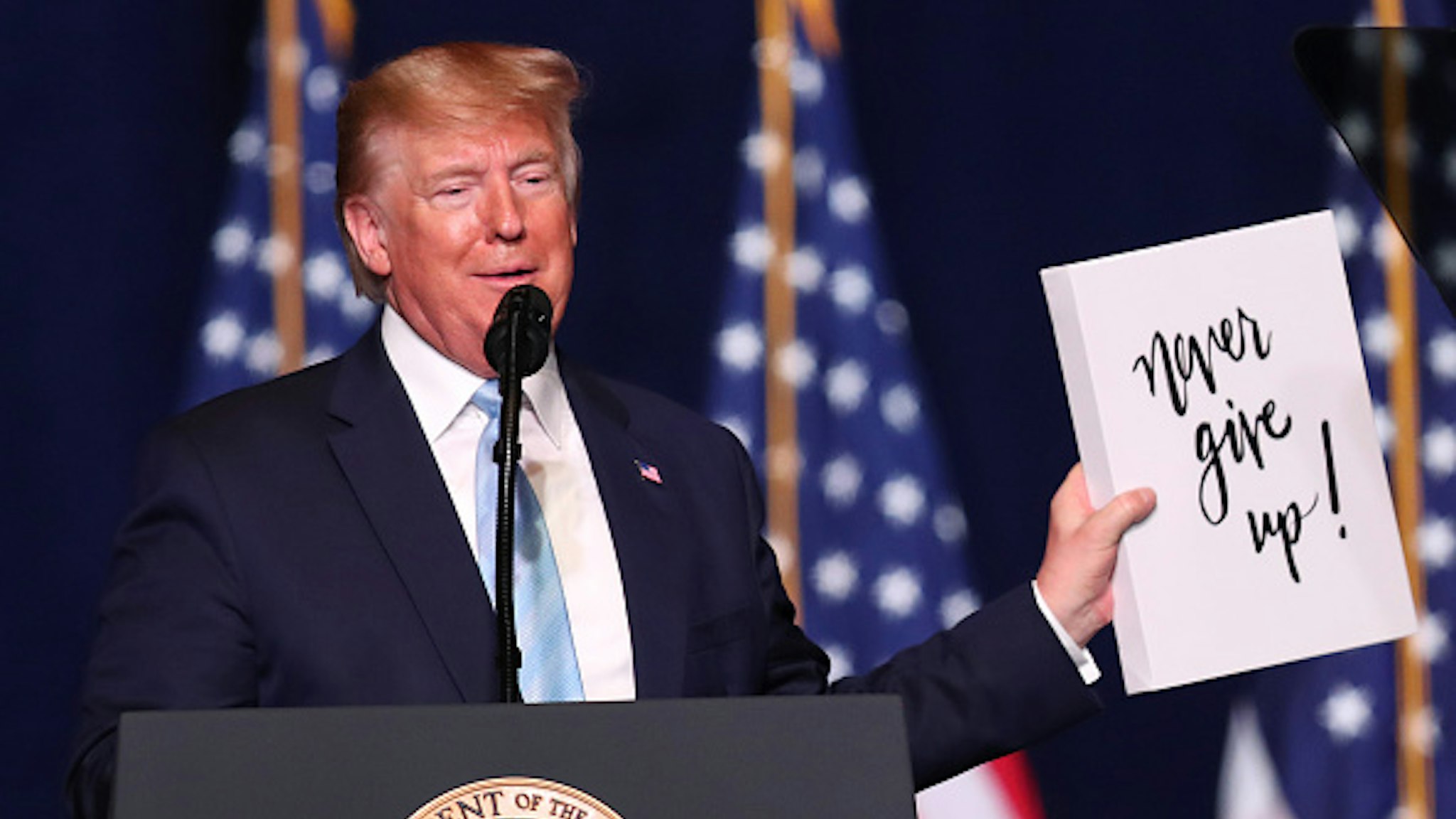 MIAMI, FLORIDA - JANUARY 03: President Donald Trump holds up a sign reading, 'never give up!,' given to him during a 'Evangelicals for Trump' campaign event held at the King Jesus International Ministry on January 03, 2020 in Miami, Florida. The rally was announced after a December editorial published in Christianity Today called for the President Trump's removal from office.