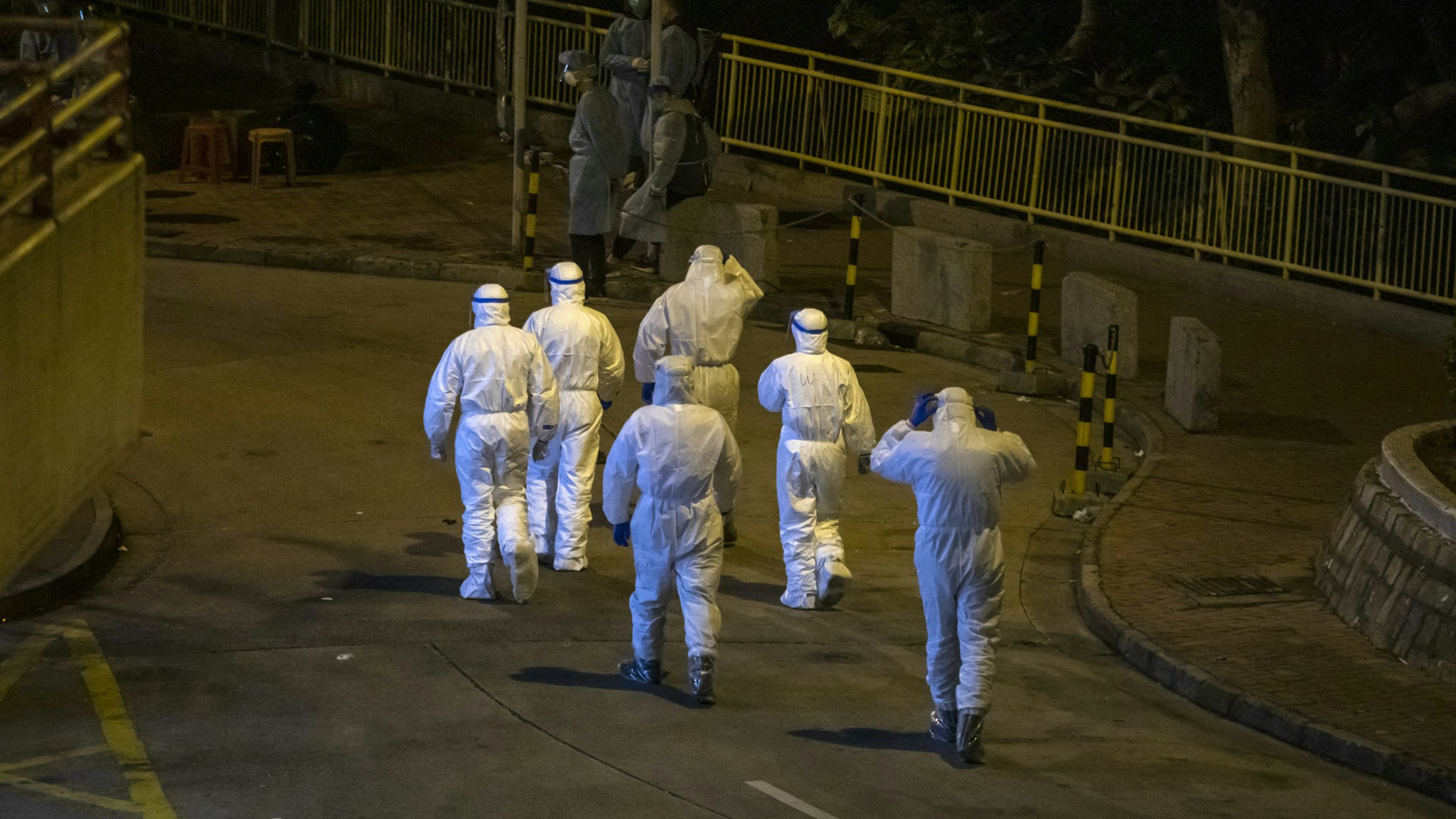 Officials wearing protective gear walk through Cheung Hong Estate in the Tsing Yi district of Hong Kong, China, in the early morning of Tuesday, Feb. 11, 2020. The Hong Kong government has evacuated some residents at a building where two patients have been confirmed to have the coronavirus infection, according to Wong Ka-Hing, controller at the Centre for Health Protection.
