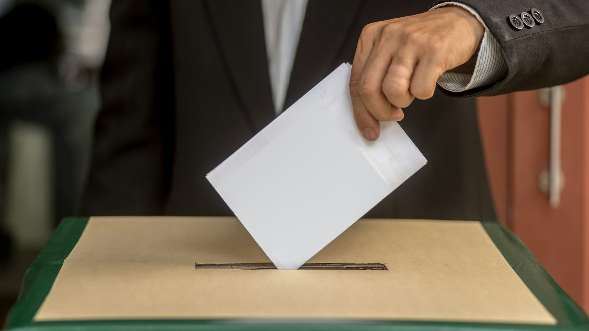 Hand of a person casting a vote into the ballot box during elections - stock photo