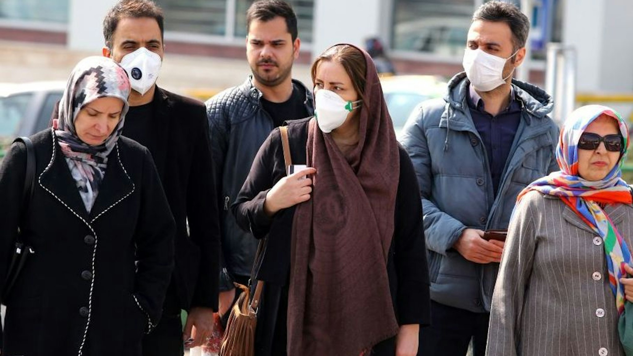 Iranians, some wearing protective masks, wait to cross a street in the capital Tehran on February 22, 2020. - Iran today reported one more death among 10 new cases of coronavirus, bringing the total number of deaths in the Islamic republic to five and infections to 28. (Photo by ATTA KENARE / AFP)