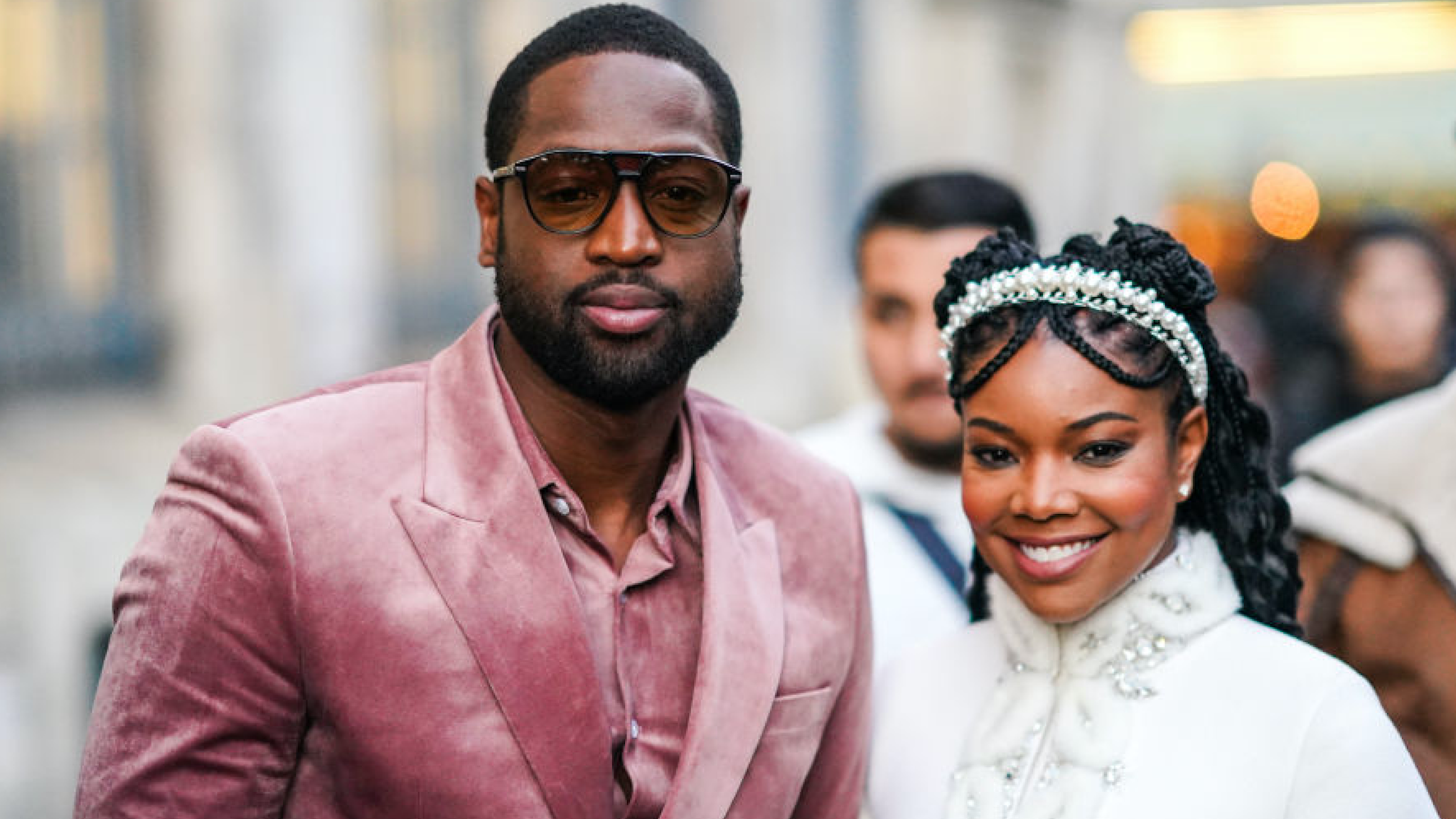 Dwayne Wade (L) wears sunglasses, a pink velvet shirt, a pink velvet jacket, a matched belt ; Gabrielle Union (R) wears a pearl headband, a white fluffy jacket with rhinestone embroideries, a mandarin collar and bell sleeves, outside Ralph & Russo, during Paris Fashion Week