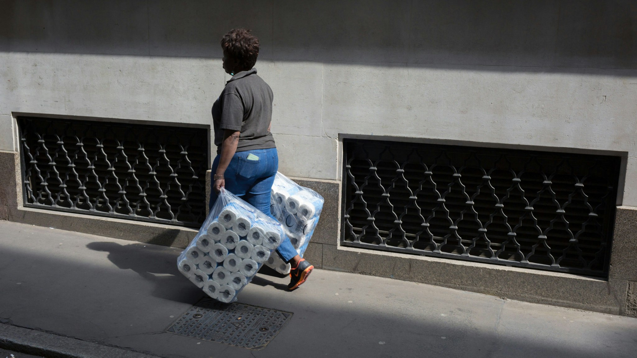 A women carries two large packs of toilet rolls into nearby offices, the capital's financial district, on 19th April, in the City of London, England.