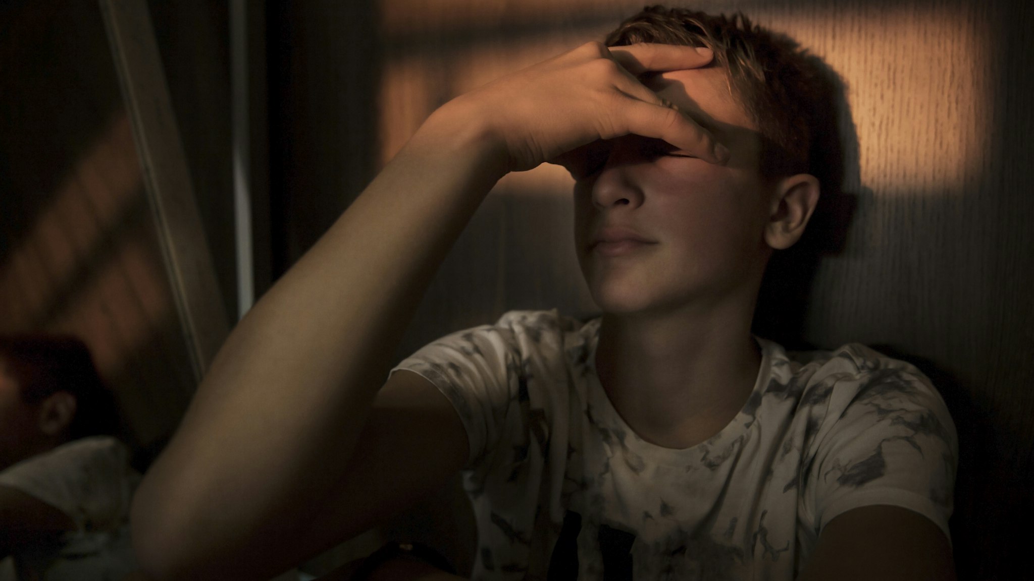 portrait of a teenager boy sitting in the dark room, with a beam of light over his eyes
