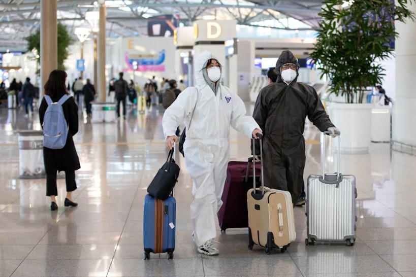 Travelers wearing protective masks and suits walk through Incheon International Airport in Incheon, South Korea, on Monday, March 9, 2020.