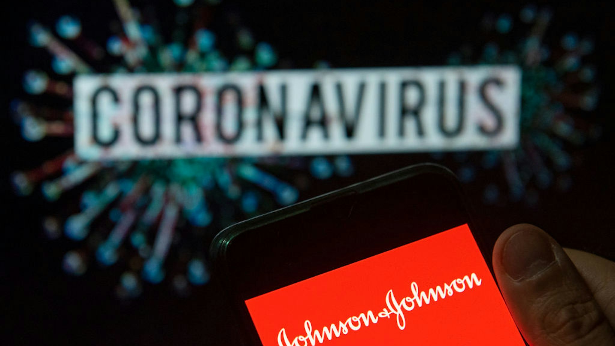 In this photo illustration the American multinational medical devices and pharmaceutical company Johnson &amp; Johnson logo seen displayed on a smartphone with a computer model of the COVID-19 coronavirus on the background.