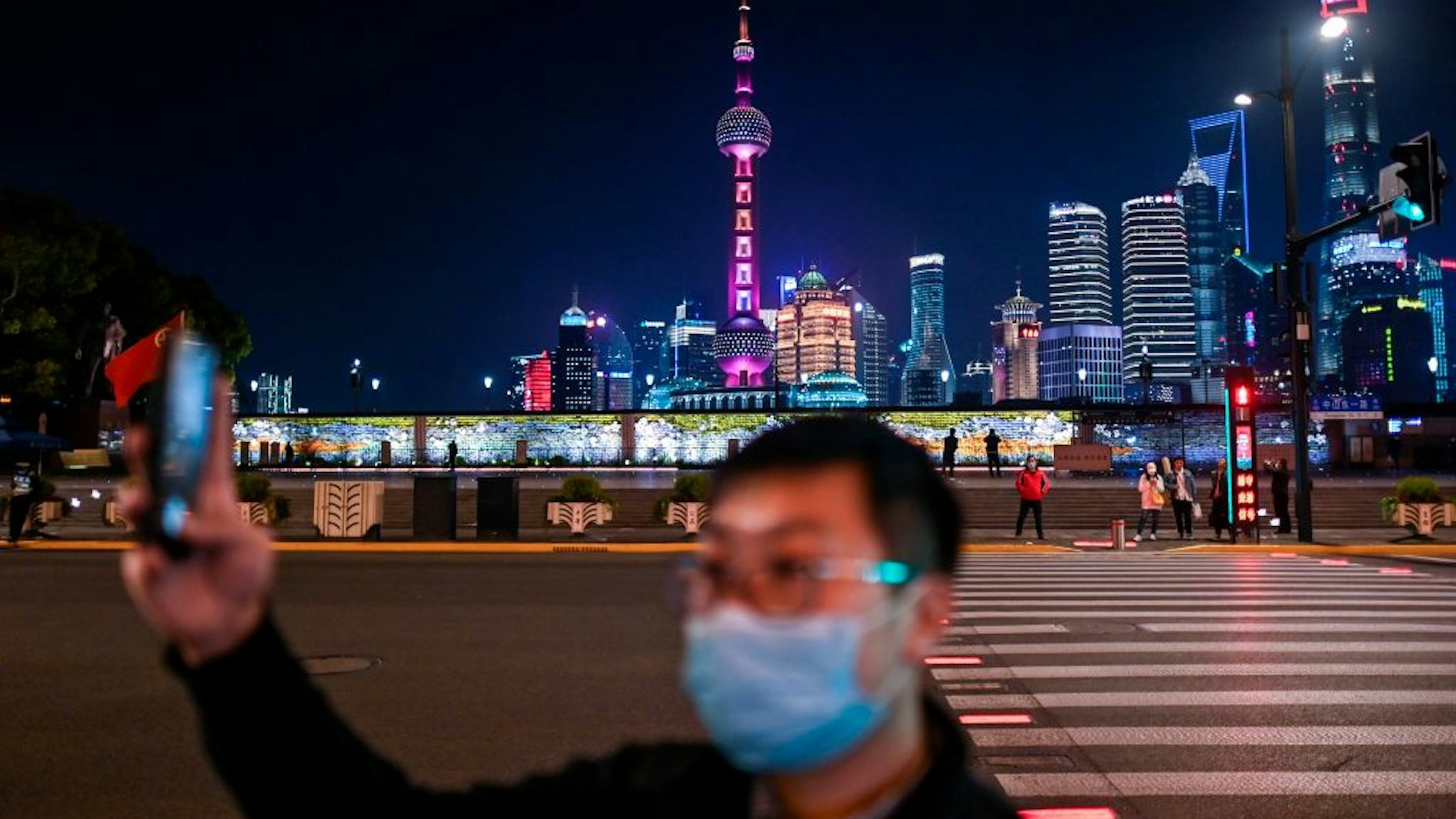 A man wearing a facemask as a preventive measure against the COVID-19 novel coronavirus takes a video of the Bund along the Huangpu River in Shanghai on March 24, 2020.