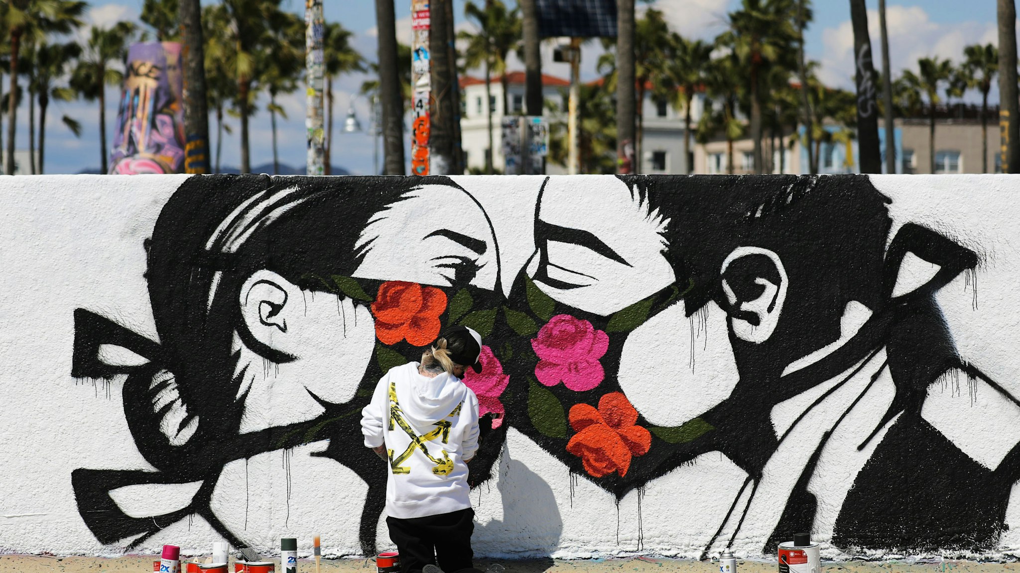 VENICE, CALIFORNIA - MARCH 21: Artist Pony Wave paints a scene depicting two people kissing while wearing face masks on Venice Beach on March 21, 2020 in Venice, California. California Governor Gavin Newsom issued a ‘stay at home’ order for California’s 40 million residents in order to slow the spread of coronavirus (COVID-19). Californians may still go to the beach without violating Newsom’s order as long as they maintain social distancing and adhere to other public health measures related to the coronavirus. (Photo by Mario Tama/Getty Images)