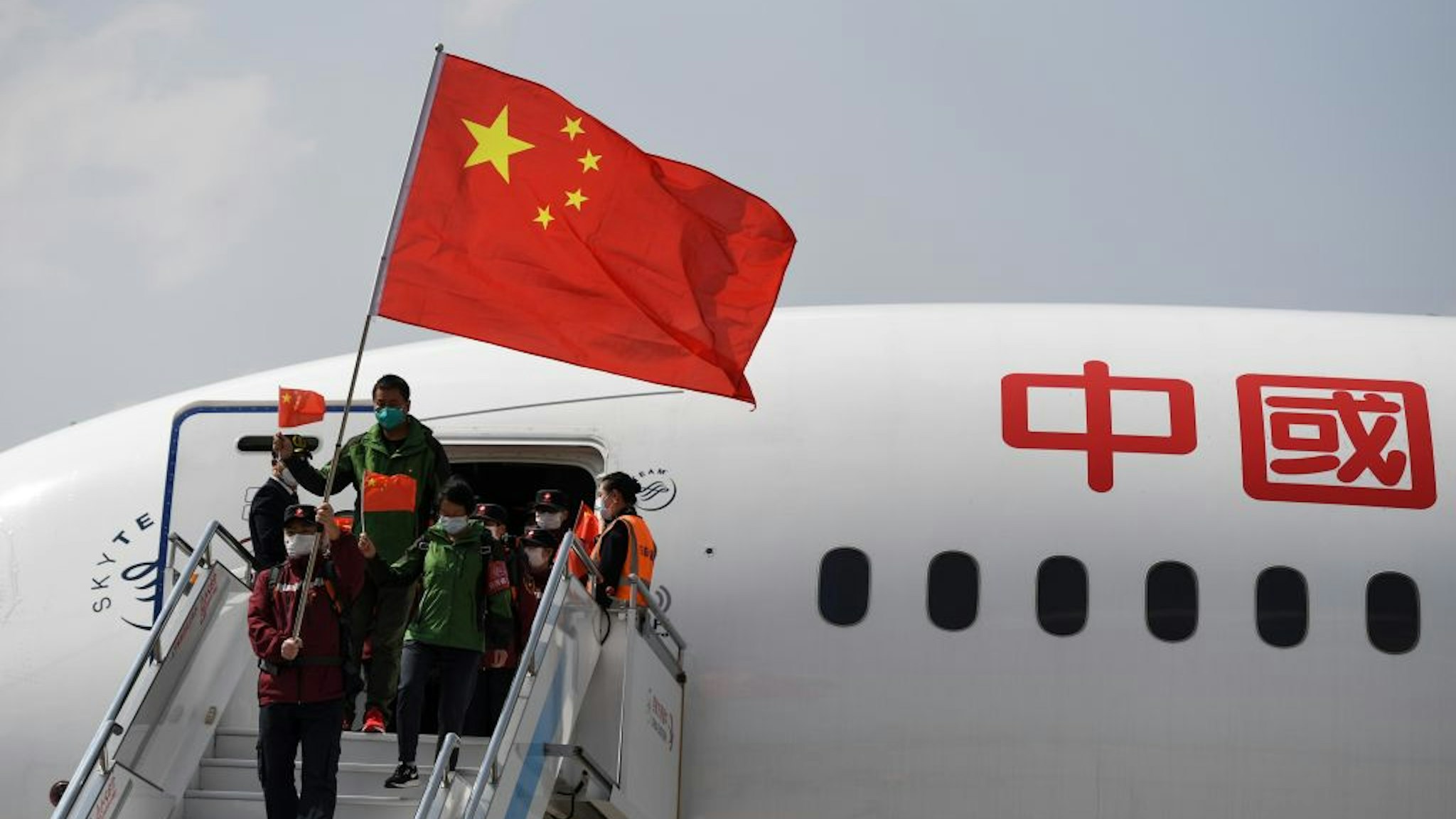Medical assistance team members holding Chinese Flags take off a plane at Kunming Changshui International Airport on March 22, 2020 in Kunming, Yunnan Province of China.