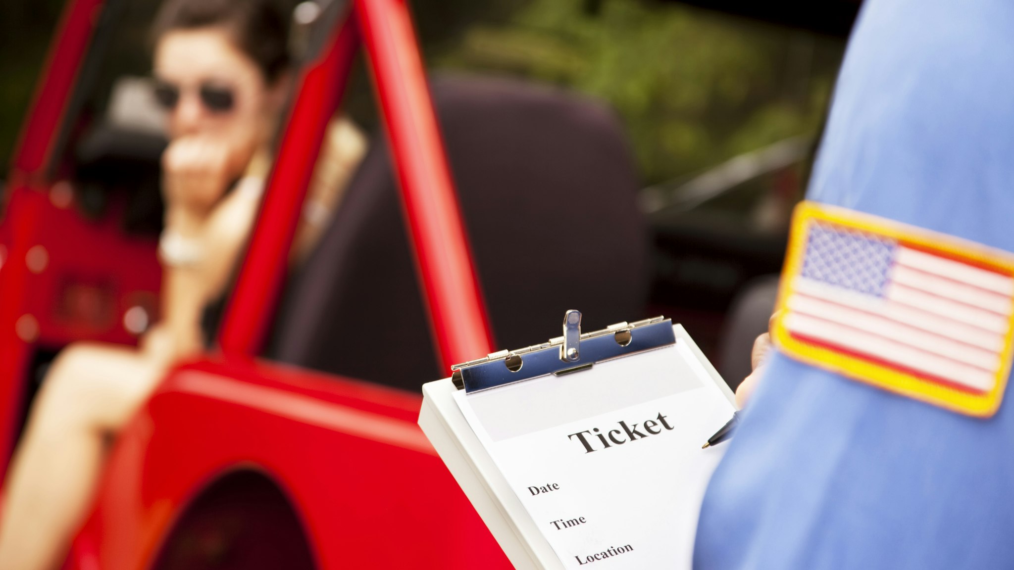 Female driver in red vehicle getting traffic ticket from policeman. - stock photo