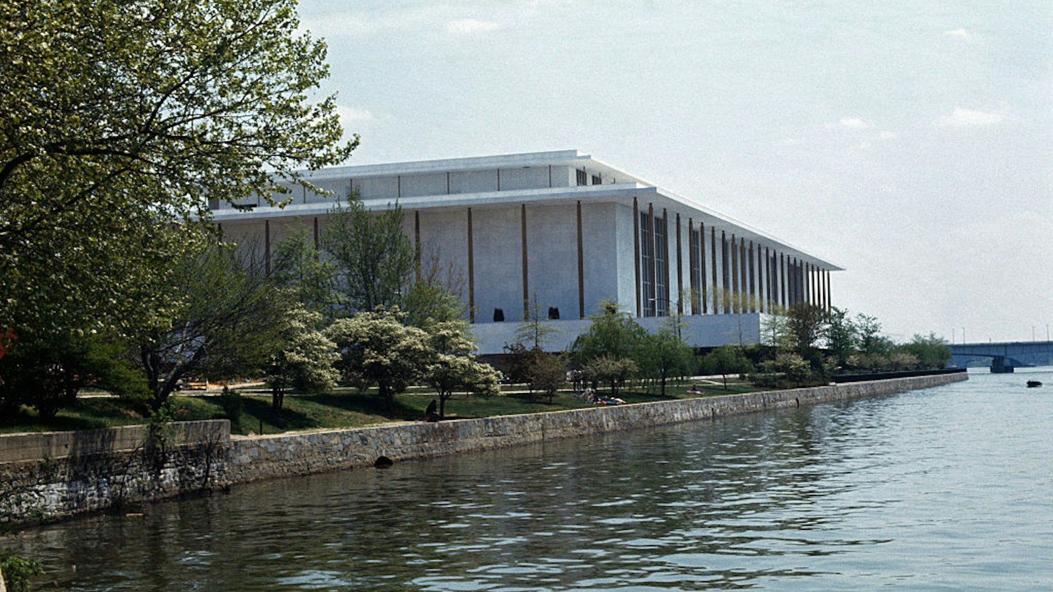 Exterior views of the John F. Kennedy Center for the Performing Arts. The building is situated at river's edge and is surrounded by trees.
