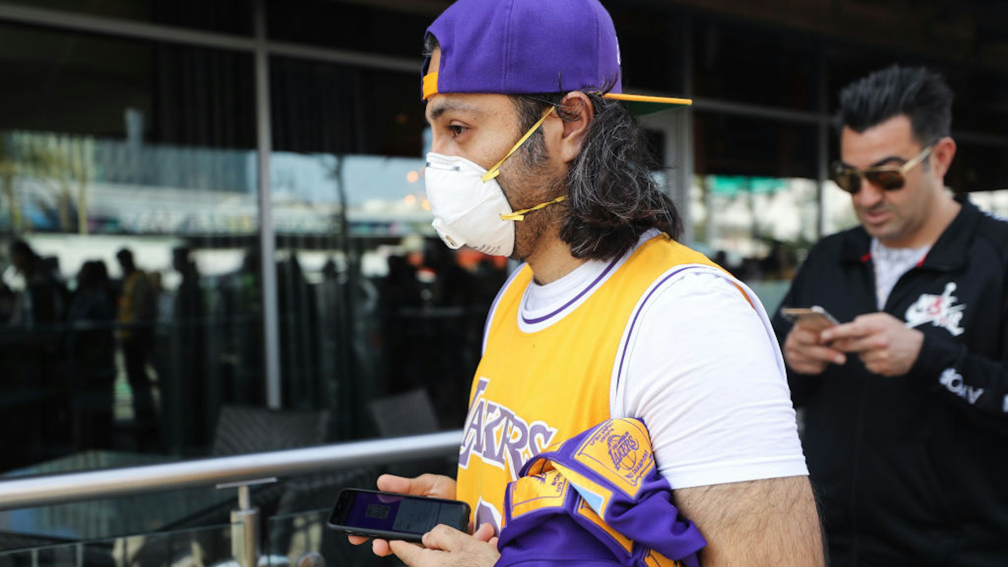 A fan wears a protective mask as people wait in line to attend the ‚ÄòCelebration of Life for Kobe and Gianna Bryant‚Äô memorial service at Staples Center on February 24, 2020 in Los Angeles, California. Los Angeles Lakers NBA star Kobe Bryant, 41, and his 13-year-old daughter Gianna were killed along with seven others in a helicopter crash near Los Angeles on January 26. (Photo by Mario Tama/Getty Images)
