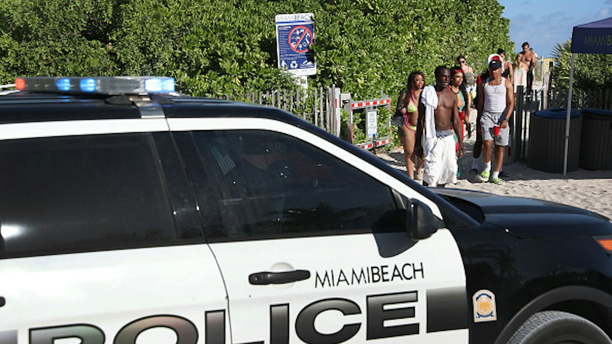 MIAMI BEACH, FLORIDA - MARCH 15: Beach goers walk past a police car as they exit from South Beach as the city closes it after 5pm in an effort to prevent the spread of the coronavirus on March 15, 2020 in Miami Beach, Florida. Miami Beach city officials temporarily closed the beach popular with college spring breakers and asked them to refrain from large gatherings where COVID-19 could spread.