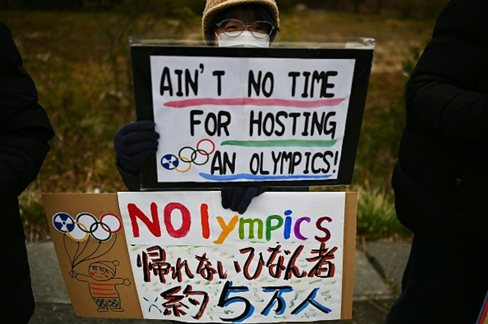 This photo taken on February 29, 2020 shows a protester holding placards during a demonstration against the Olympics, Prime Minister Shinzo Abe and nuclear energy, near the "J-Village" which will host the start of the Olympic torch relay in Naraha, Fukushima prefecture. - Tokyo 2020 CEO Toshiro Muto said on February 26 the torch relay scheduled to begin March 26 in Fukushima and travel across the country would not be cancelled, though he acknowledged adjustments might be necessary, due to the COVID-19 outbreak.