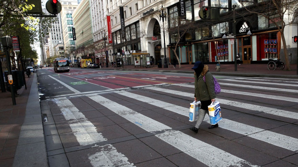A pedestrian carries two packages of toilet paper as she crosses an empty Market Street on March 17, 2020 in San Francisco, California. Seven San Francisco Bay Area counties have ordered residents to shelter in place in an effort to reduce social interaction and slow the spread of COVID-19. (Photo by Justin Sullivan/Getty Images)