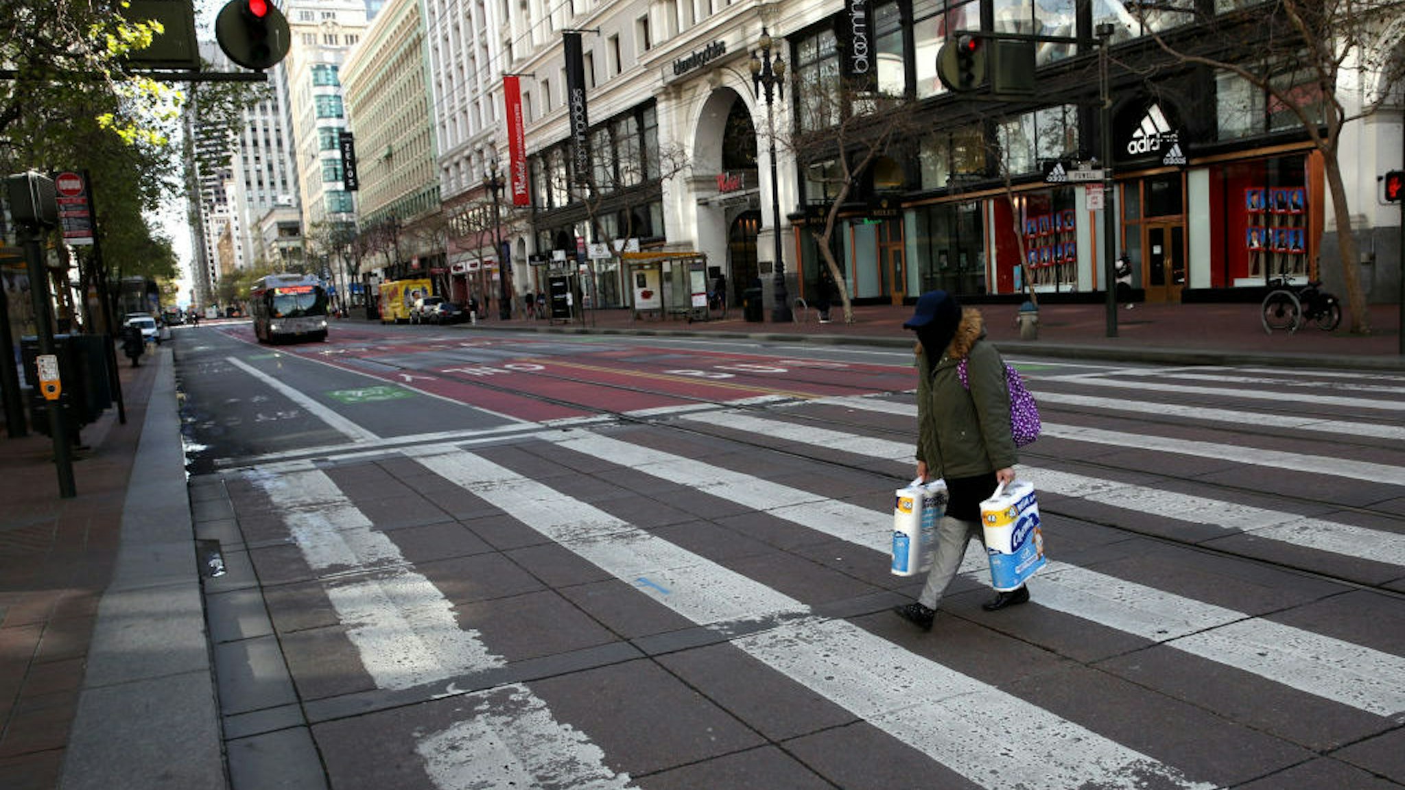 A pedestrian carries two packages of toilet paper as she crosses an empty Market Street on March 17, 2020 in San Francisco, California. Seven San Francisco Bay Area counties have ordered residents to shelter in place in an effort to reduce social interaction and slow the spread of COVID-19. (Photo by Justin Sullivan/Getty Images)