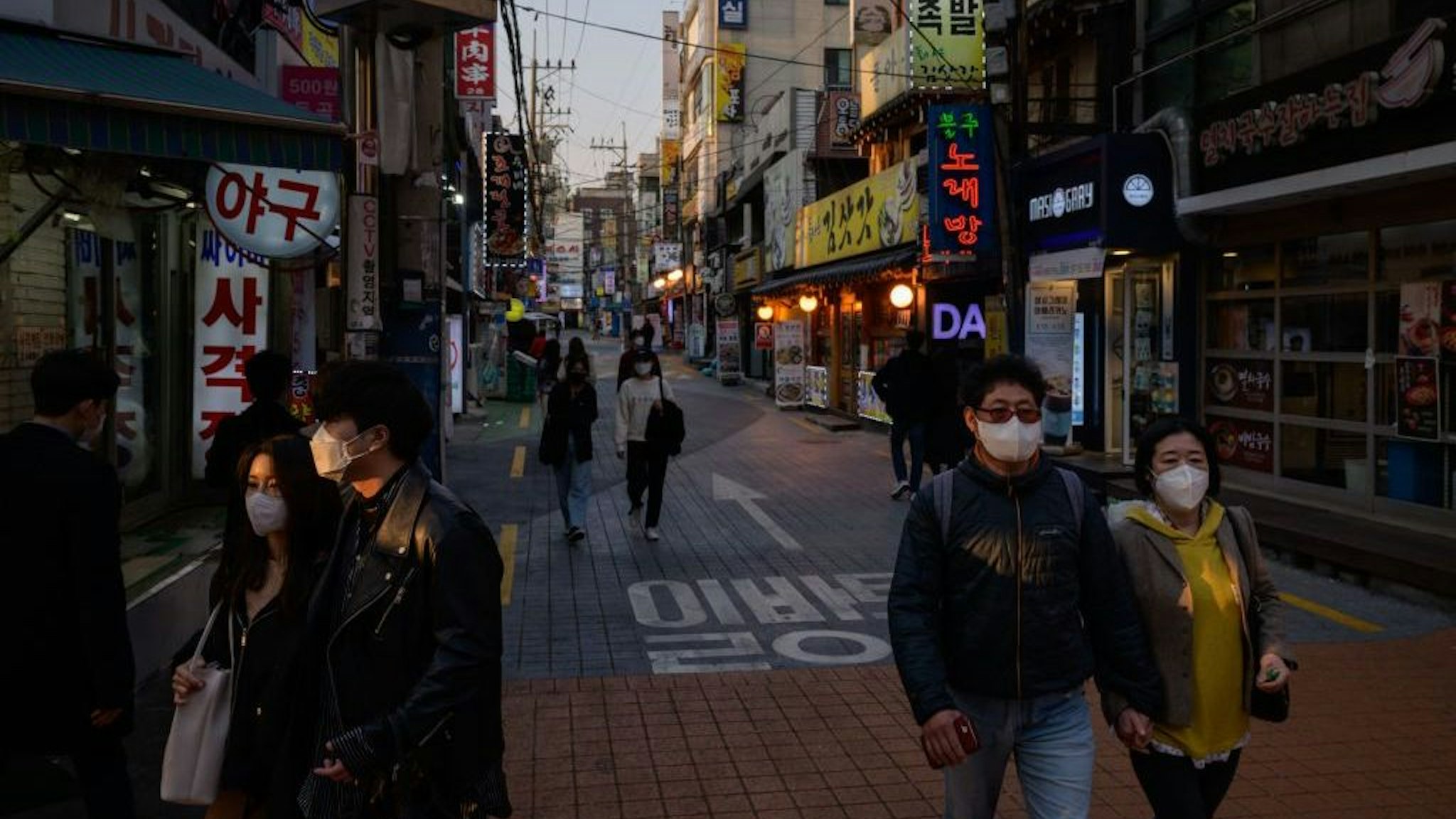 People wearing face masks amid concerns over the COVID-19 novel coronavirus, walk through an alleyway in Seoul on Marh 24, 2020. (Photo by Ed JONES / AFP)