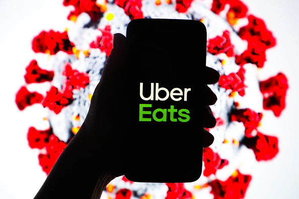 Uber Eats logo is displayed on a mobile phone screen photographed on SARS-CoV-2 illustration graphic background. Krakow, Poland on 11th March, 2020.