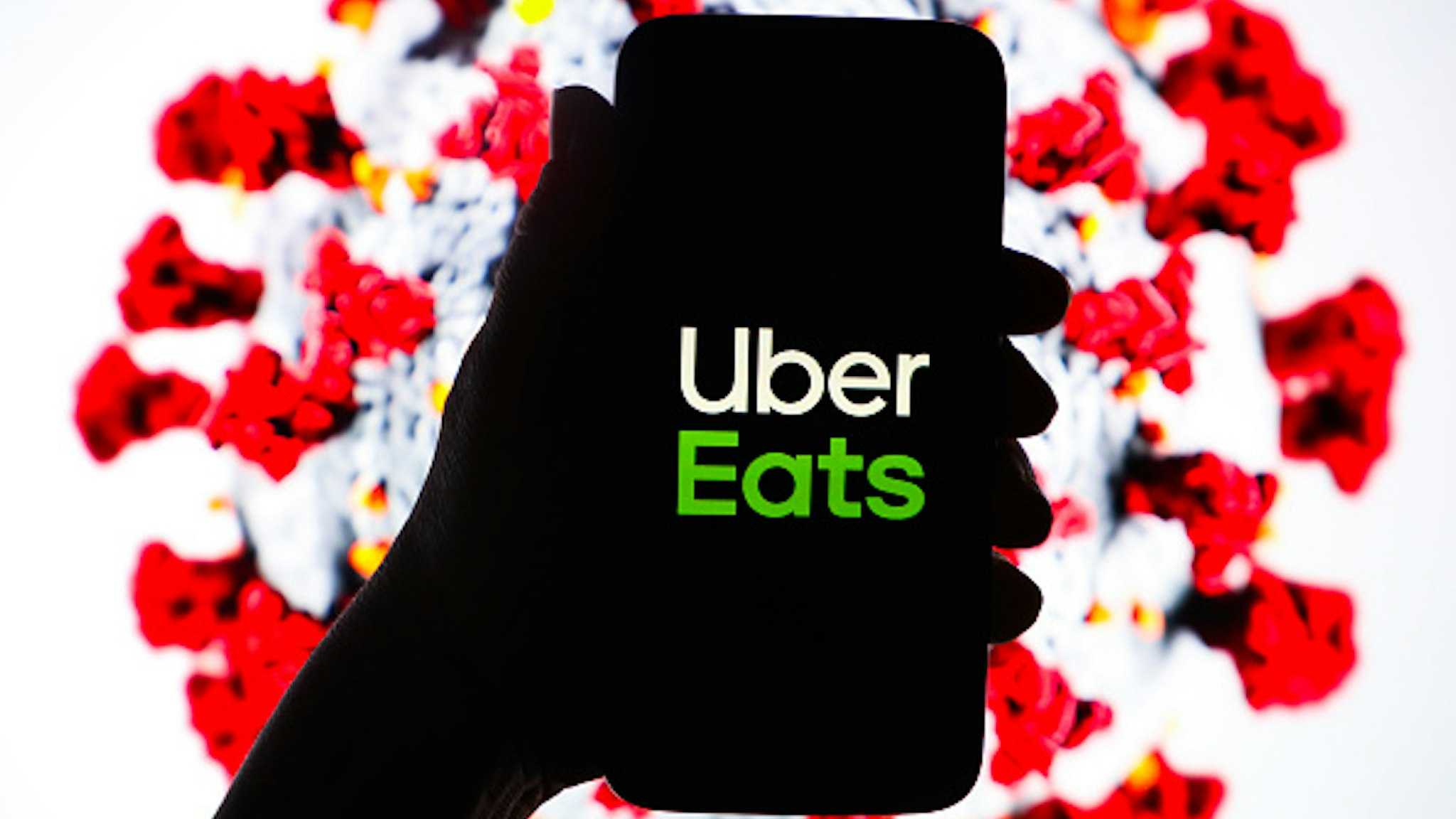 Uber Eats logo is displayed on a mobile phone screen photographed on SARS-CoV-2 illustration graphic background. Krakow, Poland on 11th March, 2020.