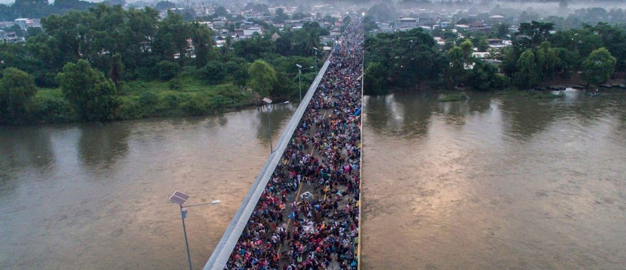 TOPSHOT - Aerial view of a Honduran migrant caravan heading to the US, on the Guatemala-Mexico international border bridge in Ciudad Hidalgo, Chiapas state, Mexico, on October 20, 2018. - Thousands of migrants who forced their way through Guatemala's northwestern border and flooded onto a bridge leading to Mexico, where riot police battled them back, on Saturday waited at the border in the hope of continuing their journey to the United States. (Photo by PEDRO PARDO / AFP) (Photo credit should read