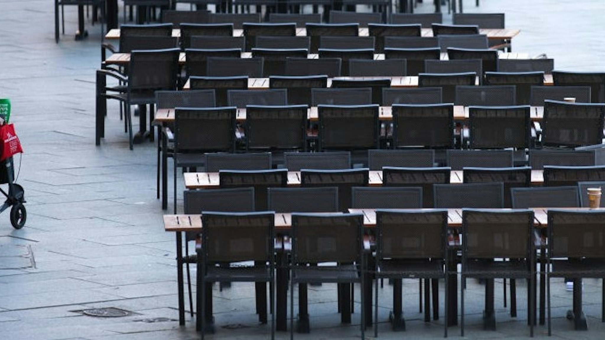 18 March 2020, North Rhine-Westphalia, Cologne: A woman walks past empty tables of a cafe in Cologne. Due to the spread of the coronavirus, many catering establishments are closed indefinitely. Photo: Thomas Banneyer/dpa (Photo by