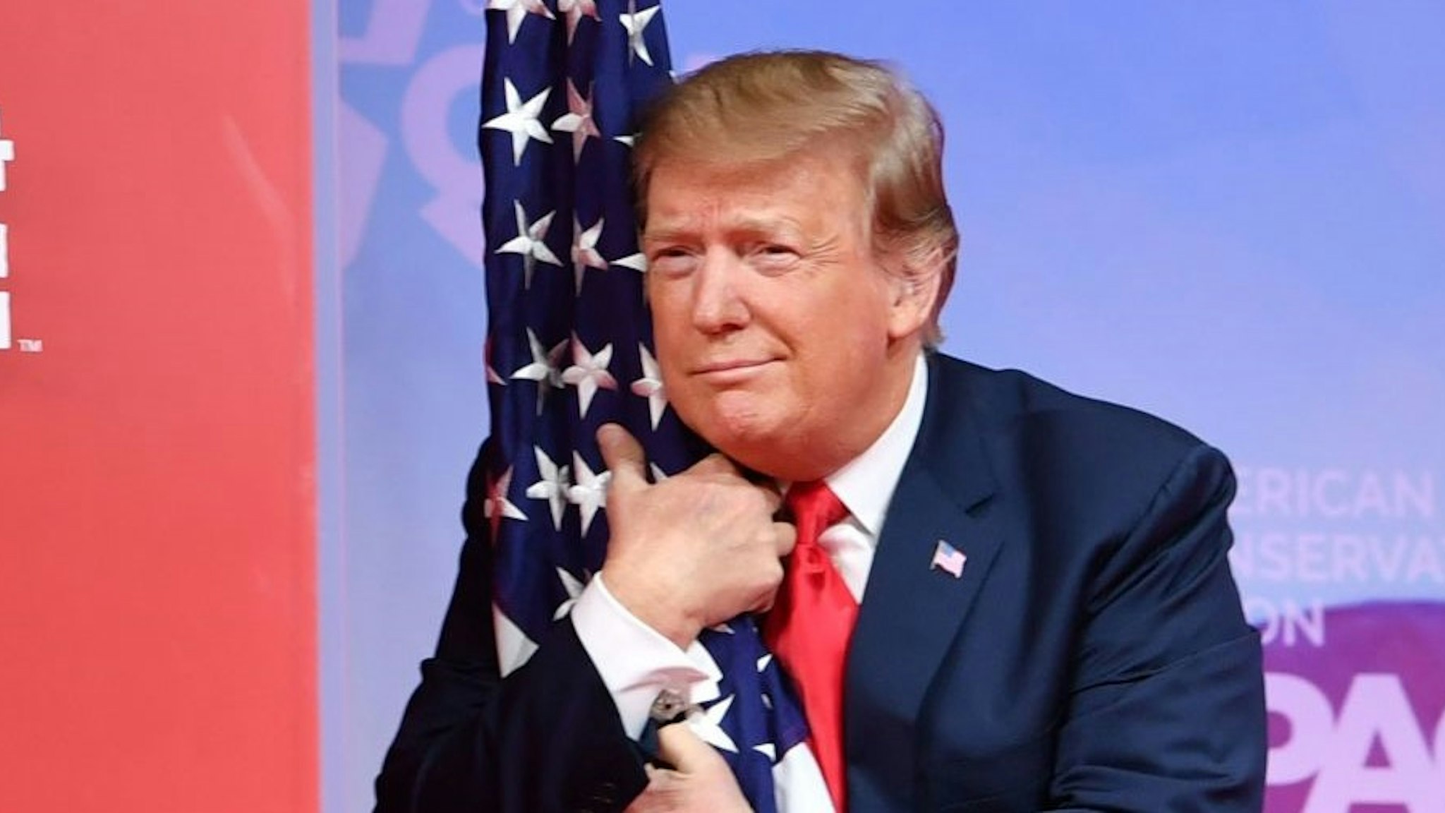TOPSHOT - US President Donald Trump hugs the US flag as he arrives to speak at the annual Conservative Political Action Conference (CPAC) in National Harbor, Maryland, on March 2, 2019. (Photo by NICHOLAS KAMM / AFP) / ALTERNATIVE CROP (Photo by