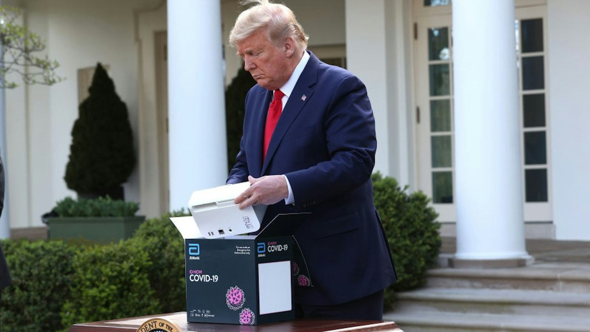 WASHINGTON, DC - MARCH 30: U.S. President Donald Trump takes a new COVID-19 test kit developed by Abbott Labs out of its box during the daily coronavirus briefing at the Rose Garden of the White House on March 30, 2020 in Washington, DC. The United States has updated its guidelines to U.S. citizens to maintain current social distancing practices through the end of April after the number of reported coronavirus (COVID-19) deaths doubled to over 2,000 nationwide within two days. (Photo by