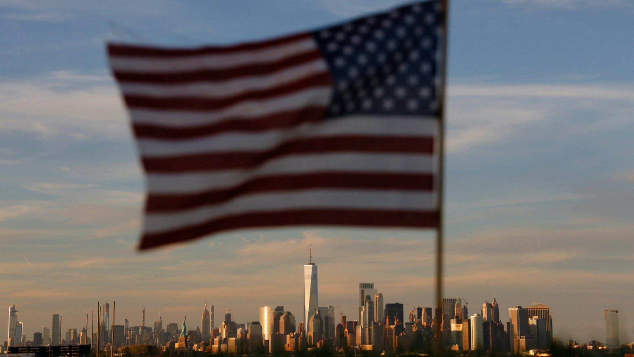 The sun sets on the skyline of lower Manhattan, the Statue of Liberty and the Empire State Building in New York City as an American flag flies at the Tear Drop 9/11 Memorial on June 9, 2019 in Bayonne, New Jersey.
