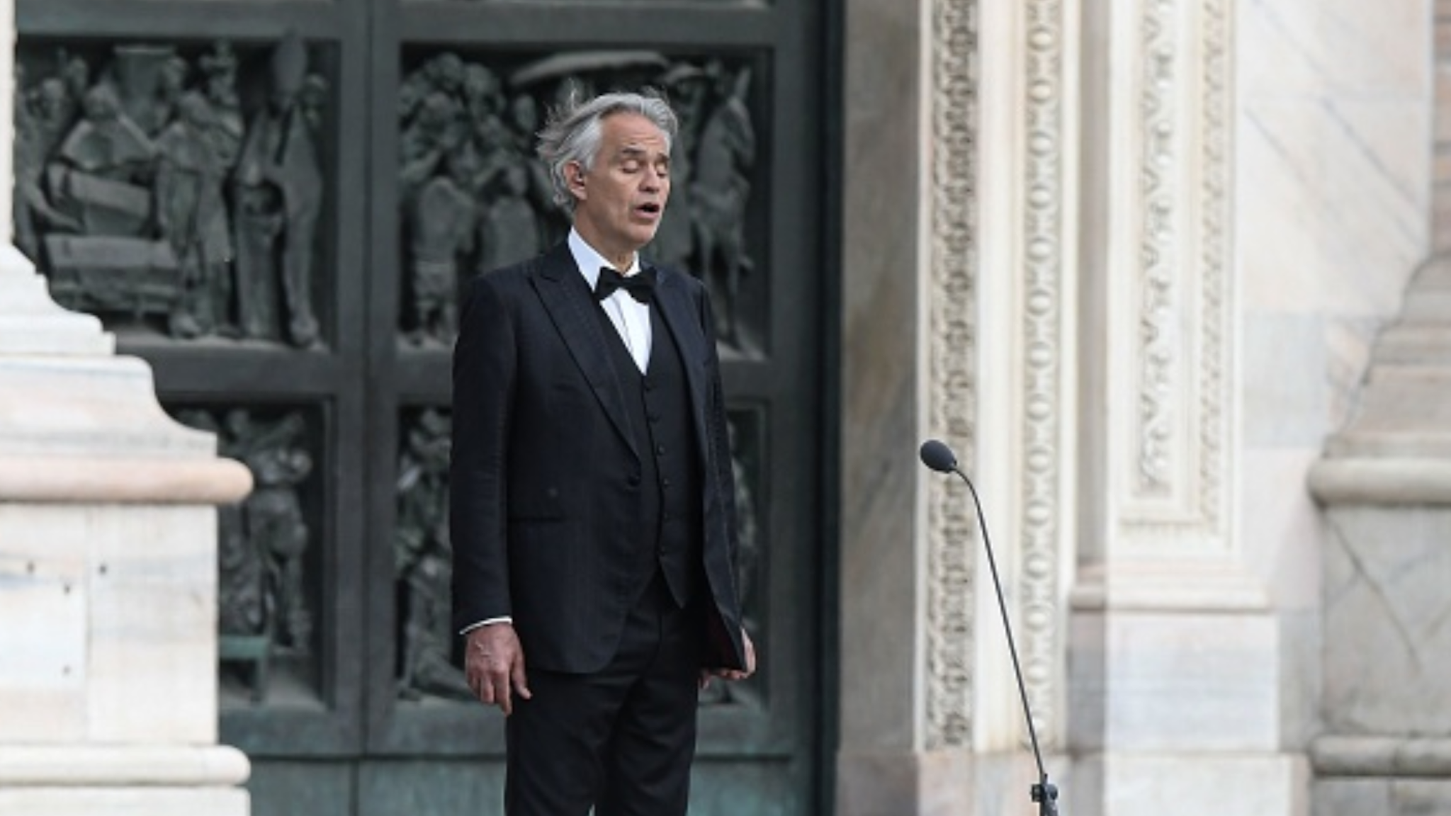 TOPSHOT - Italian tenor and opera singer Andrea Bocelli sings during a rehearsal on a deserted Piazza del Duomo in central Milan on April 12, 2020, prior to an evening performance without public for the world wounded by the pandemic, during the country's lockdown aimed at curbing the spread of the COVID-19 infection, caused by the novel coronavirus.