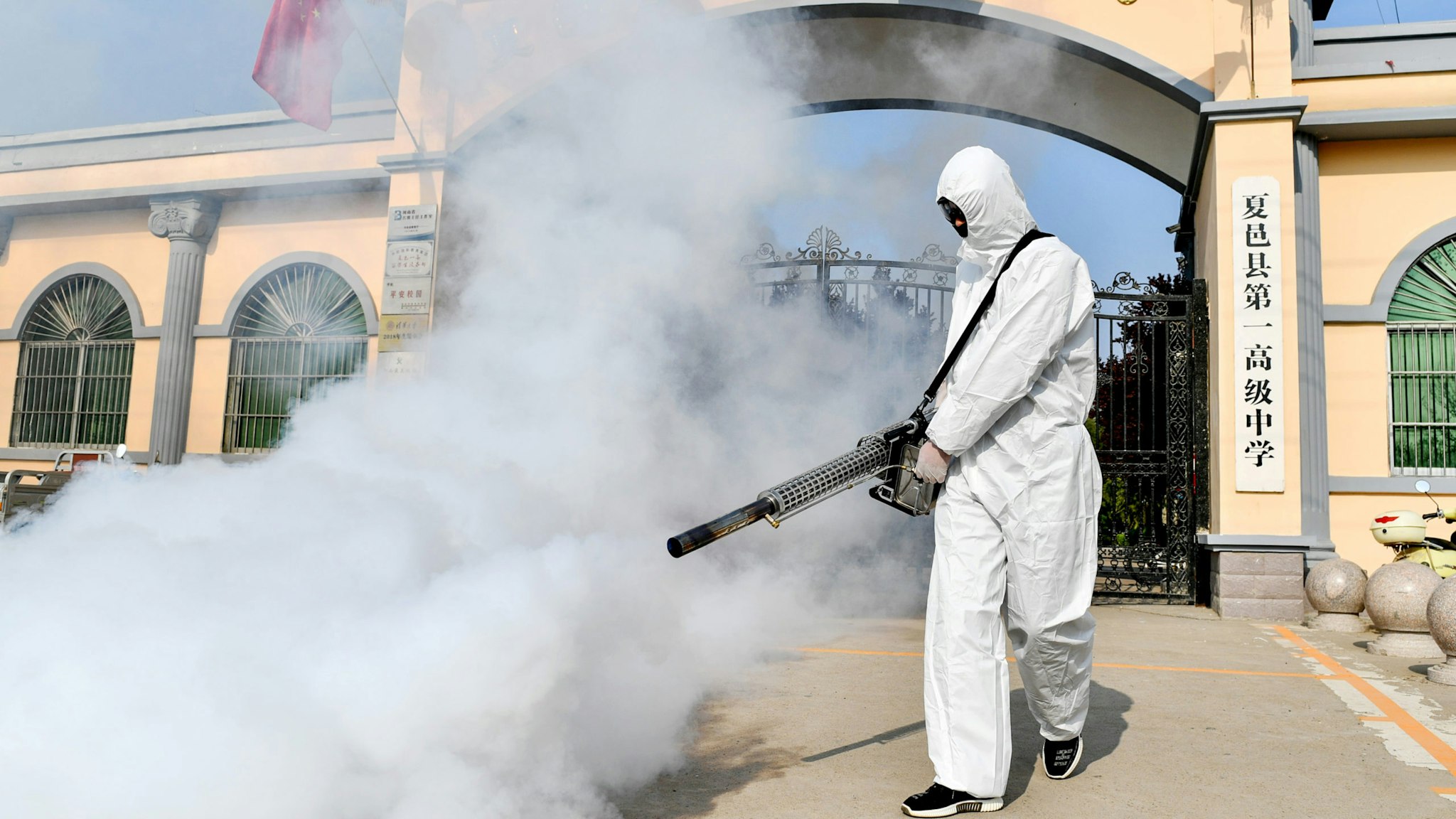A volunteer sprays disinfectant at a school as the school prepares for students returning after the term opening was delayed due to the COVID-19 coronavirus outbreak, in Shangqiu in China's central Henan province on April 3, 2020.