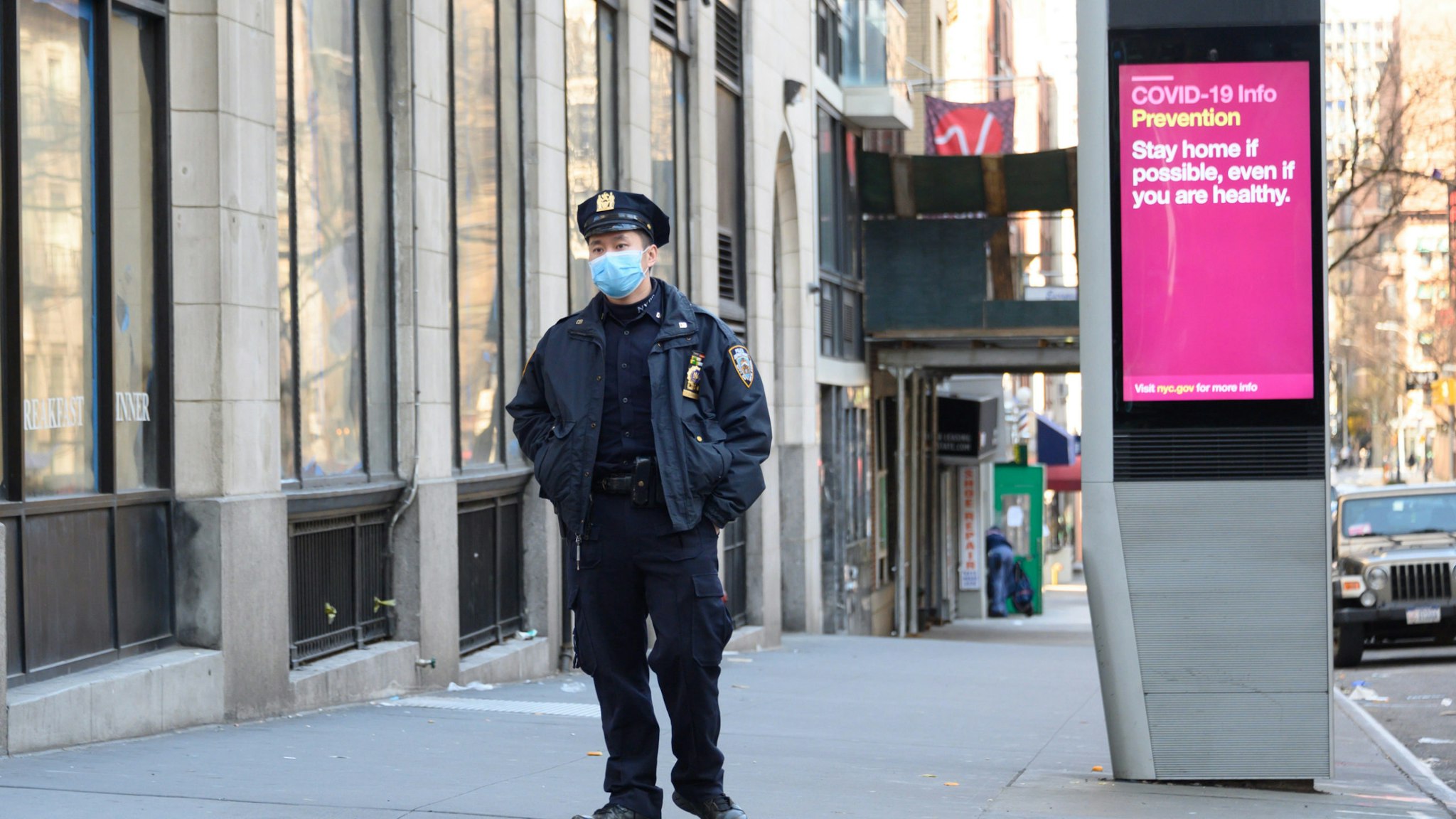 An NYPD police officer is seen wearing a protective face mask next to a LinkNYC screen with information related to COVID-19 as the coronavirus continues to spread across the United States on March 27, 2020 in New York City.