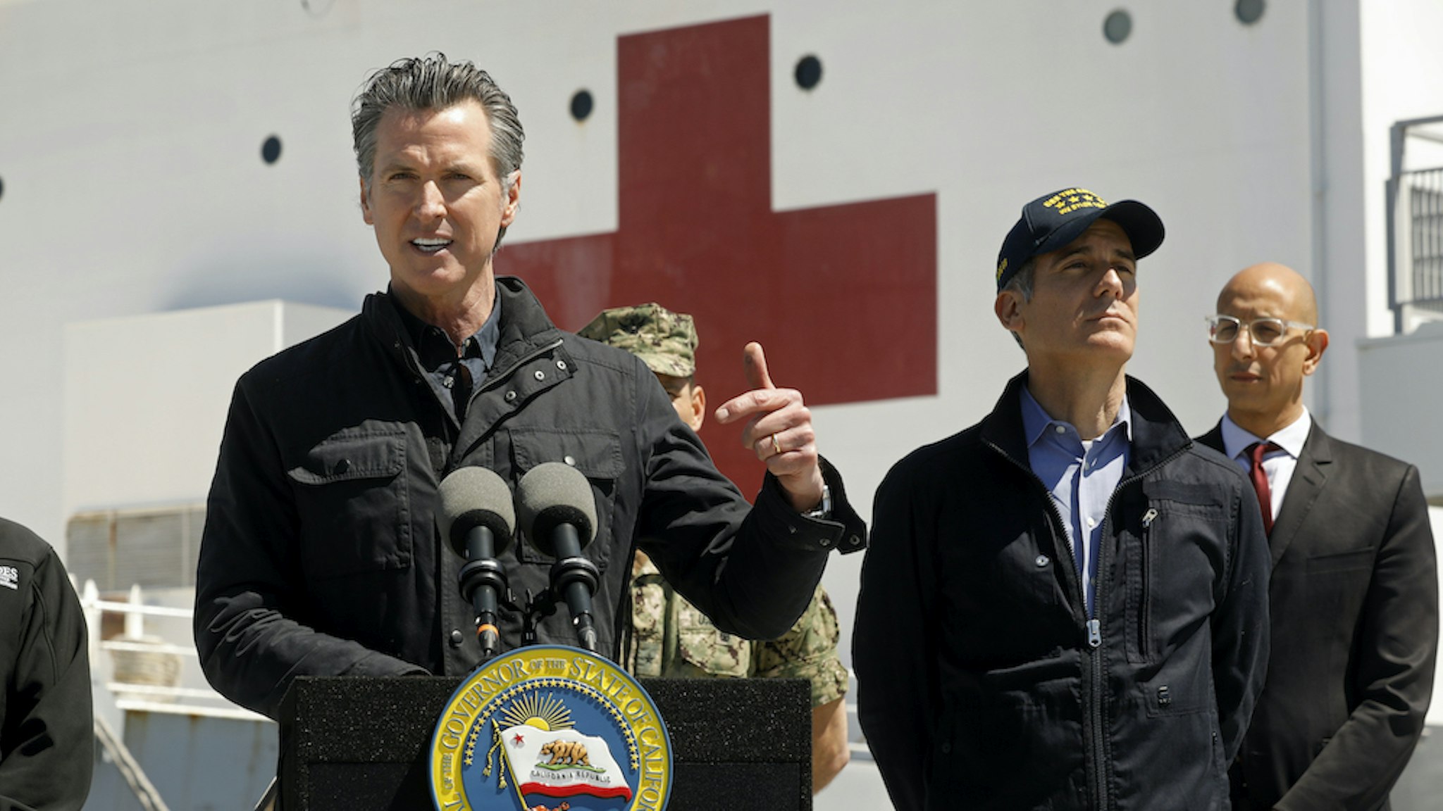 California Governor Gavin Newsom speaks in front of the hospital ship USNS Mercy that arrived into the Port of Los Angeles on Friday, March 27, 2020, to provide relief for Southland hospitals overwhelmed by the coronavirus pandemic. Also attending the press conference were Director Mark Ghilarducci, Cal OES, left, Los Angeles Mayor Eric Garcetti, second from right, and Dr. Mark Ghaly, Secretary of Health and Human Services, far right, along with others not shown. (POOL PHOTOGRAPHS by Carolyn Cole/Los Angeles Times)