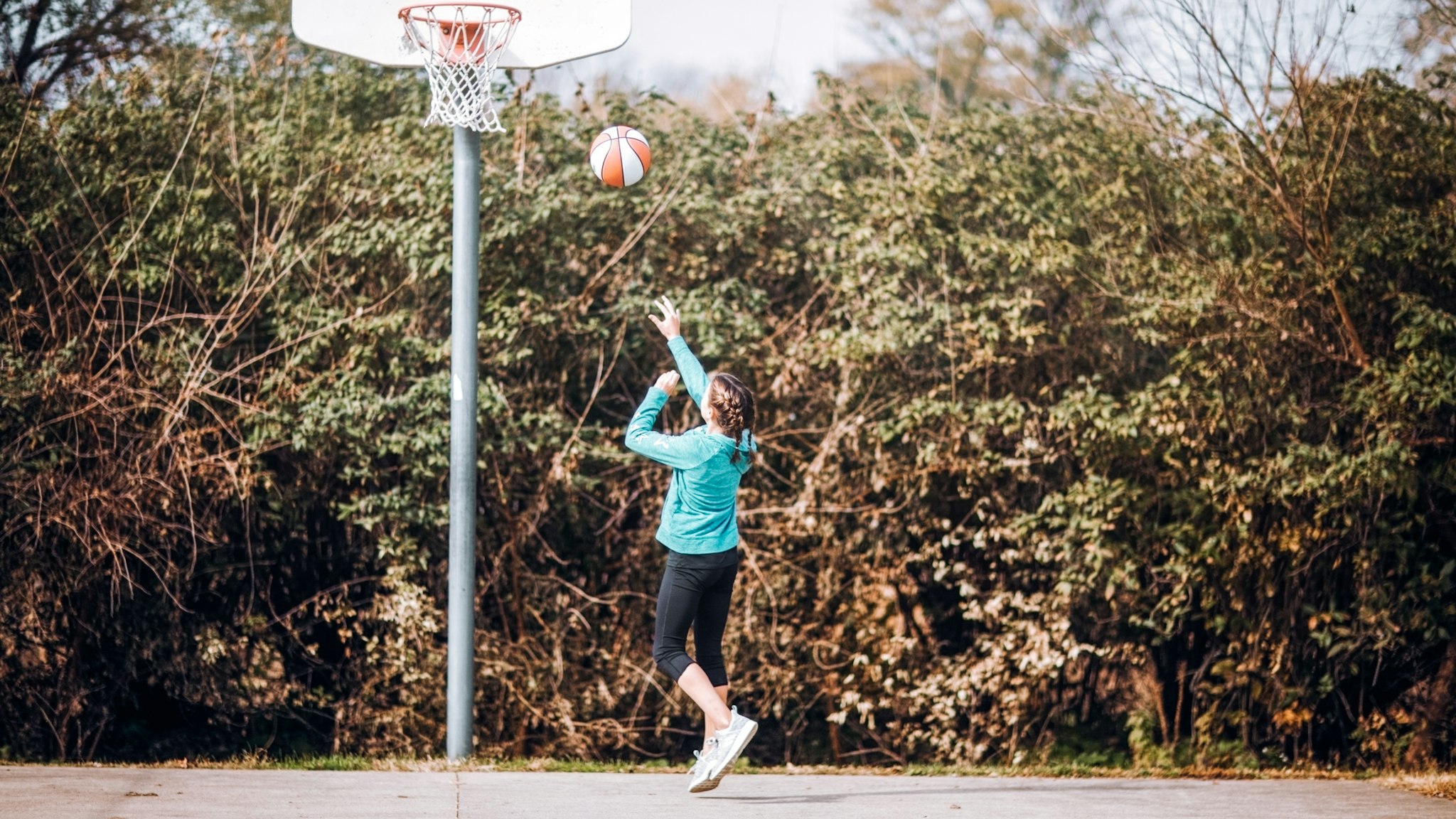 pre-teen girl shooting a layup on outdoor basketball court - stock photo