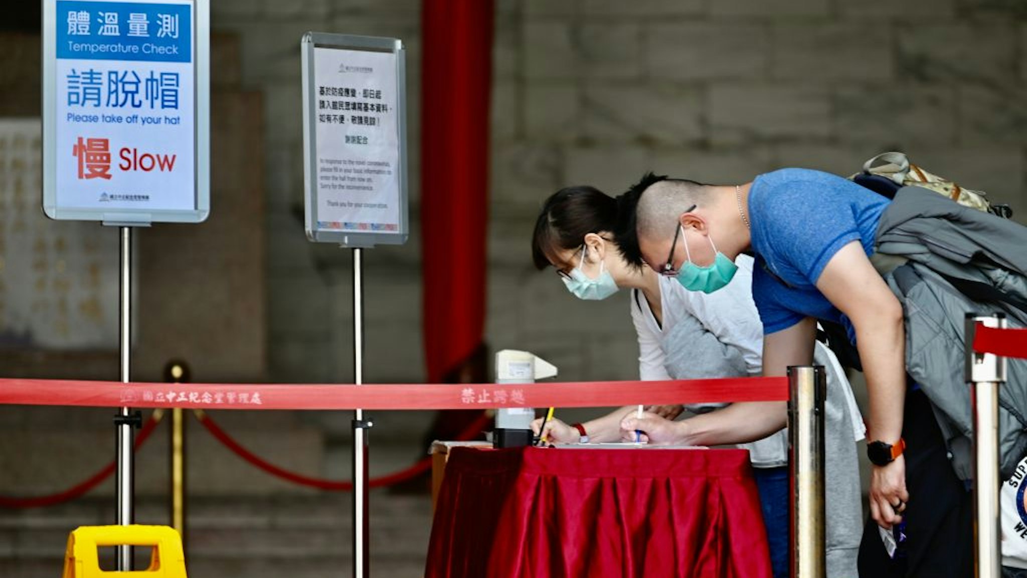 A masked couple fill in forms with personal information, amid concerns of the COVID-19 coronavirus, while visiting the Chiang Kai-shek (CKS) Memorial Hall in Taipei on March 31, 2020