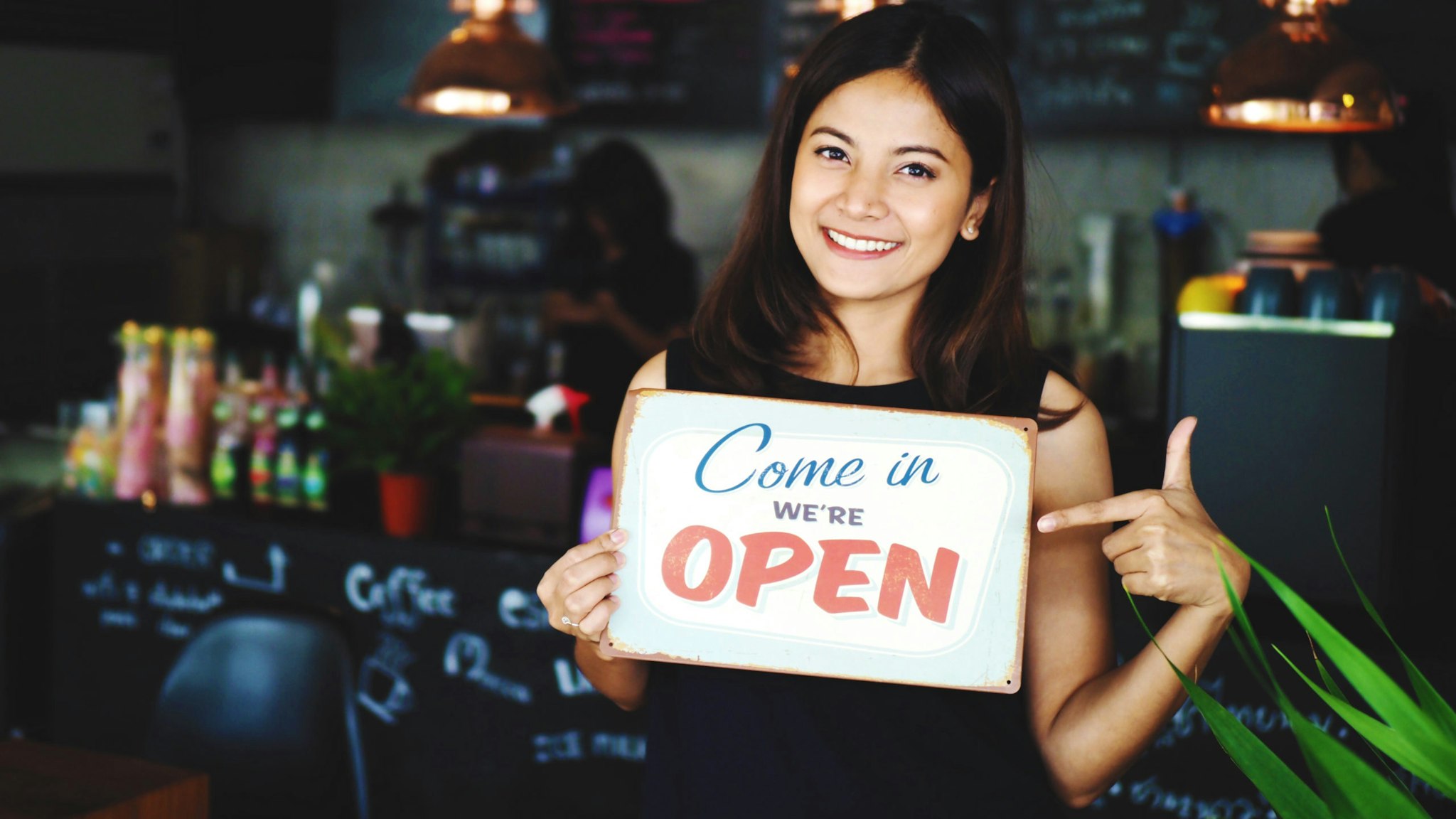 Portrait Of Smiling Young Woman Holding Open Sign While Standing In Cafe - stock photo