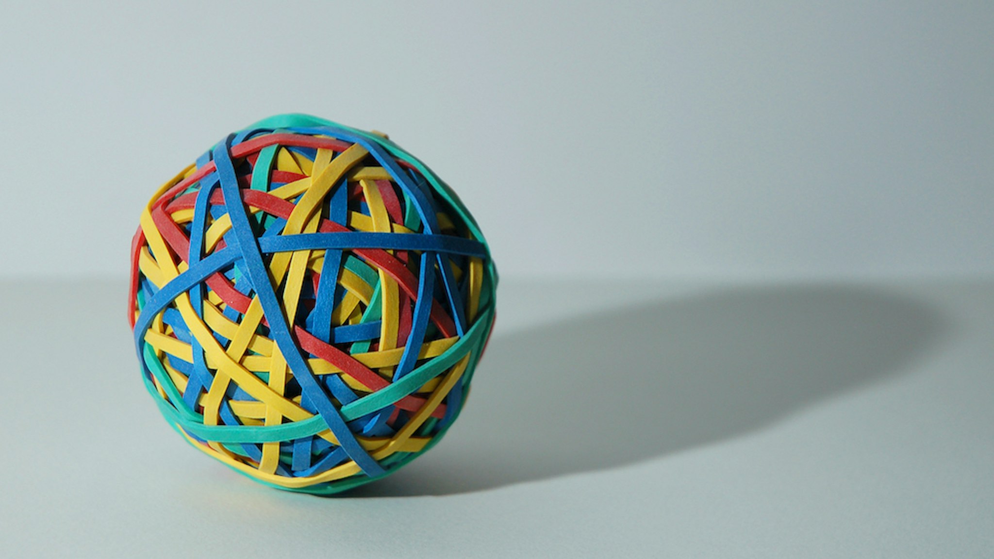 Multicolor rubber band ball on solid gray background.