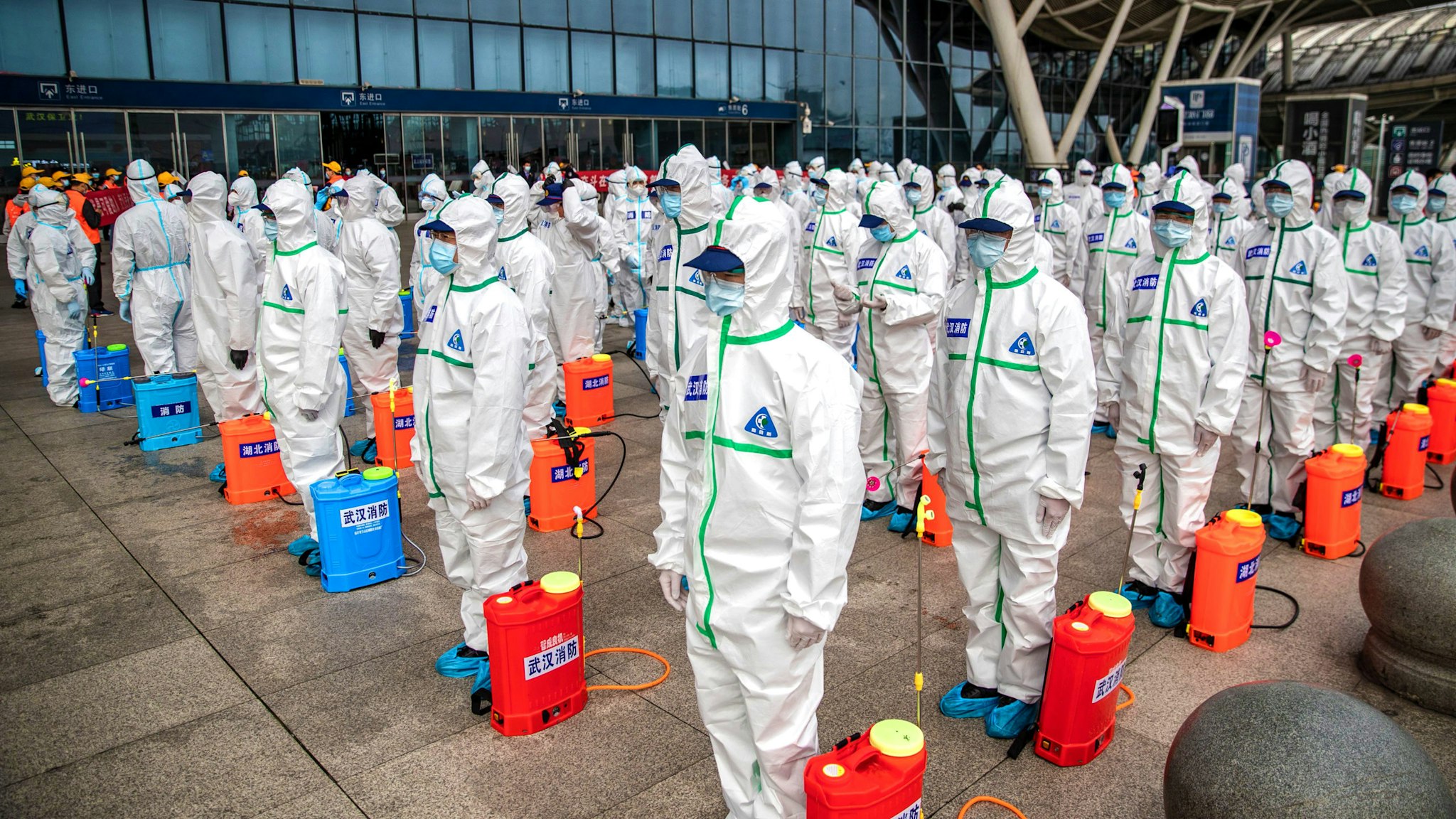 Staff members line up at attention as they prepare to spray disinfectant at Wuhan Railway Station in Wuhan in China's central Hubei province on March 24, 2020. - China announced on March 24 that a lockdown would be lifted on more than 50 million people in central Hubei province where the COVID-19 coronavirus first emerged late last year.