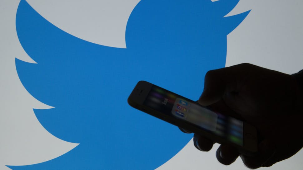 A picture shows a man holding a cellphone in front of a twitter logo in Ankara, Turkey on March 16, 2017.