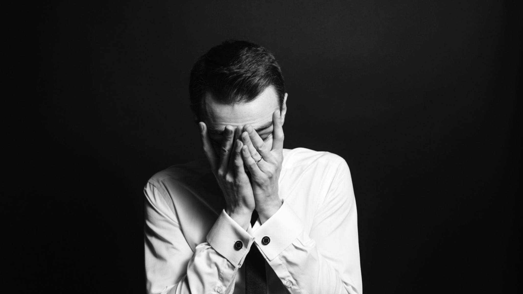 Hands over face Tired Businessman Against Black Background.