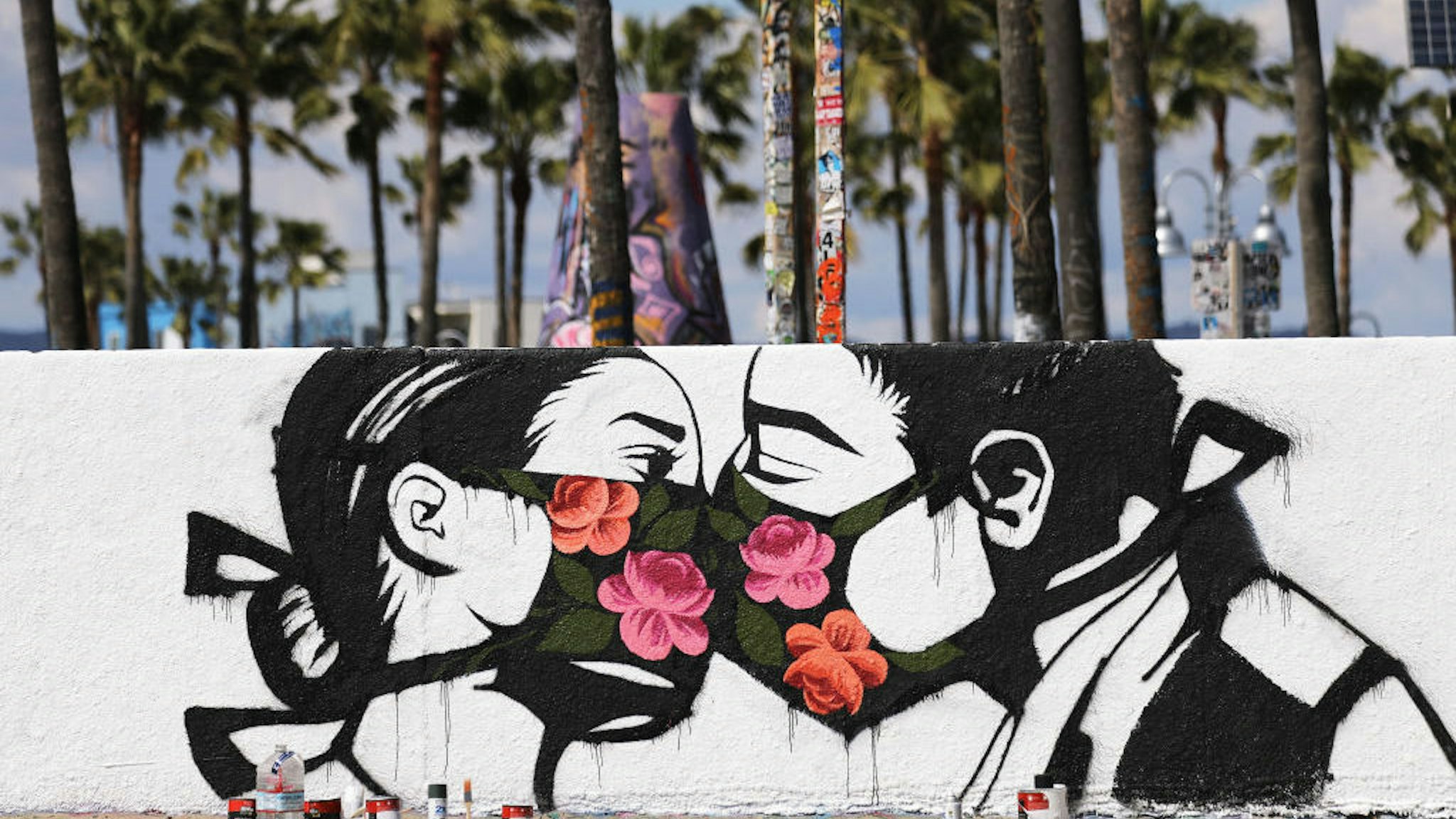 Palm trees stand behind a street art piece by artist Pony Wave depicting two people kissing while wearing face masks on Venice Beach on March 21, 2020 in Venice, California. California Governor Gavin Newsom issued a ‚Äòstay at home‚Äô order for California‚Äôs 40 million residents in order to slow the spread of coronavirus (COVID-19). Californians may still go to the beach without violating Newsom‚Äôs order as long as they maintain social distancing and adhere to other public health measures related to the coronavirus. (Photo by Mario Tama/Getty Images)