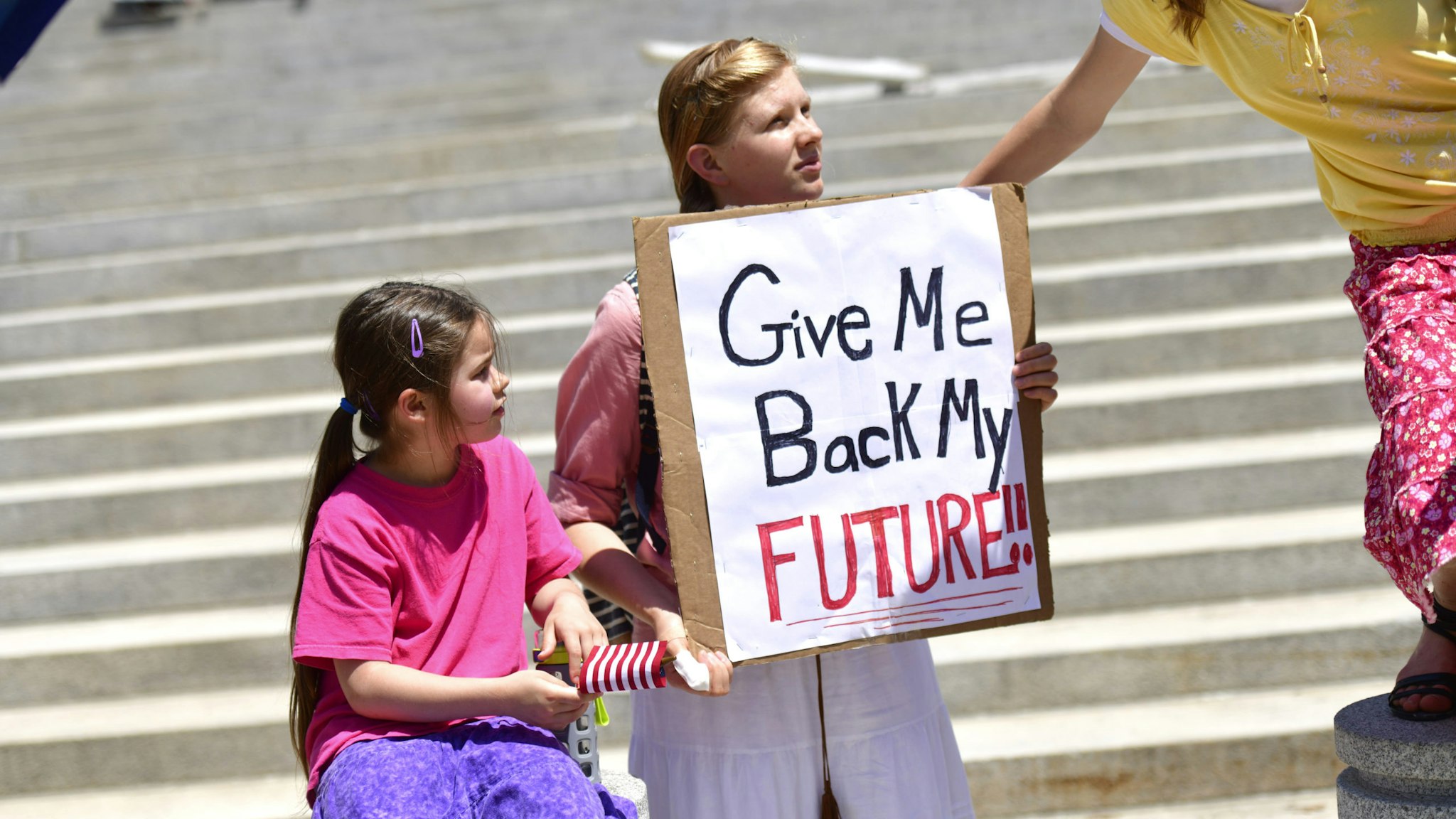 HARRISBURG, PA - MAY 15: A girl holds a placard stating "Give Me Back My Future" during a rally outside the Pennsylvania Capitol Building concerning the continued closure of businesses due to the coronavirus pandemic on May 15, 2020 in Harrisburg, Pennsylvania. Pennsylvania Governor Tom Wolf has introduced a color tiered strategy to reopen the state with most areas not easing restrictions until June 4.