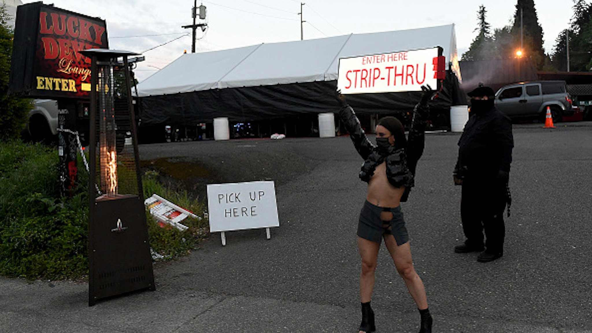 PORTLAND, OREGON - MAY 01: Dancer Nikki waves a sign in front of The Lucky Devil during the Drive-thru on May 01, 2020 in Portland, Oregon. The strip club offers drive thru dances during the Coronavirus Pandemic.